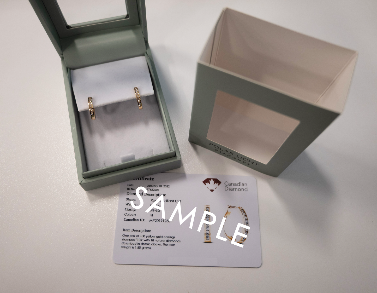 Presentation shot of 10K Yellow Gold 1/5 Cttw Diamond 1.4cm petite channel-set hoop earrings inside their branded box packaging, paired with a sample Canadian diamond ID certificate.