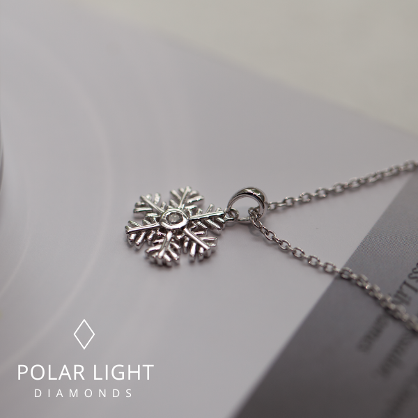 Close up of sterling silver Canadian diamond snowflake pendant necklace on a light gray background with rolo chain and 'Polar Light Diamonds' branding.