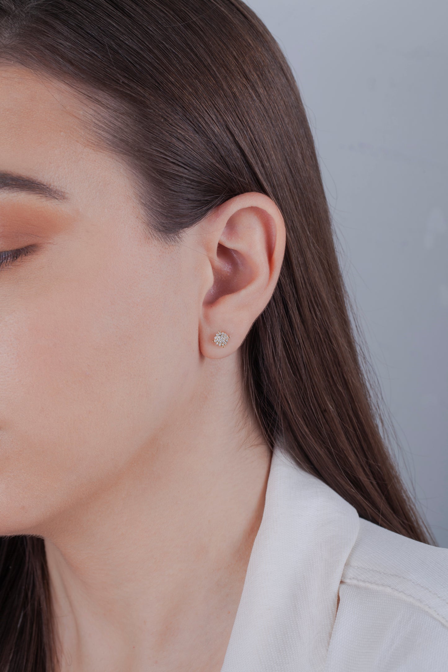 Close-up of a person wearing a 10k yellow gold cluster diamond earring with a neutral background