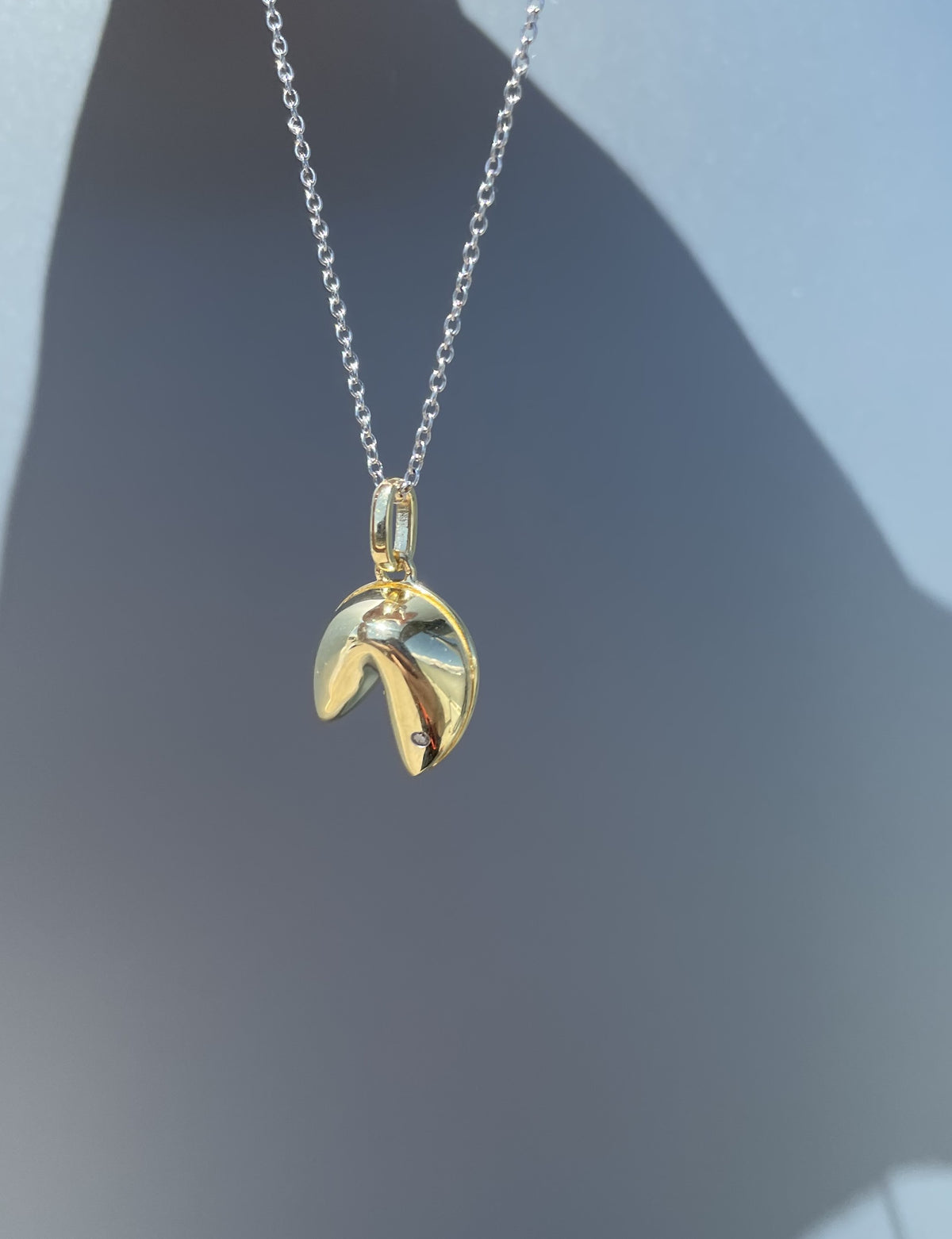 Close-up product view of a yellow gold plated 925 sterling silver fortune cookie pendant necklace suspended against a grey background, showcasing the highly polished finish and the single 0.01 Ct natural Canadian diamond accent set on the corner.