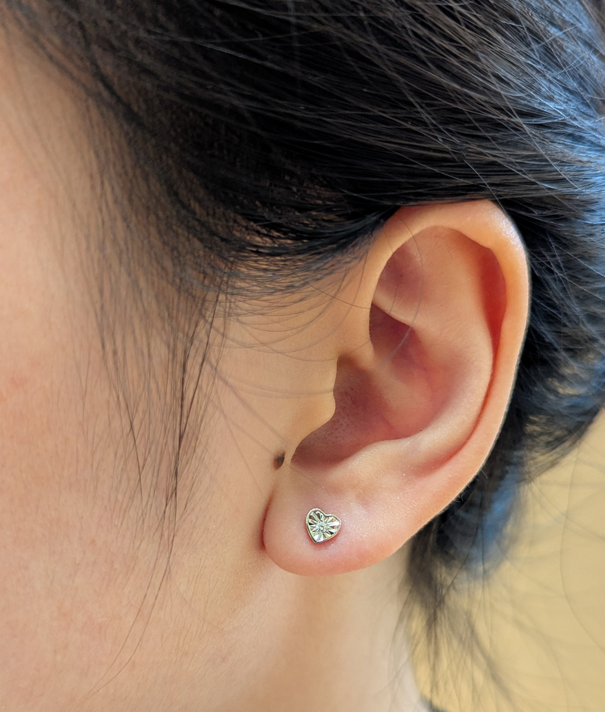 10K rose gold 0.02 cttw Canadian diamond dainty heart shaped stud earring on ear model.