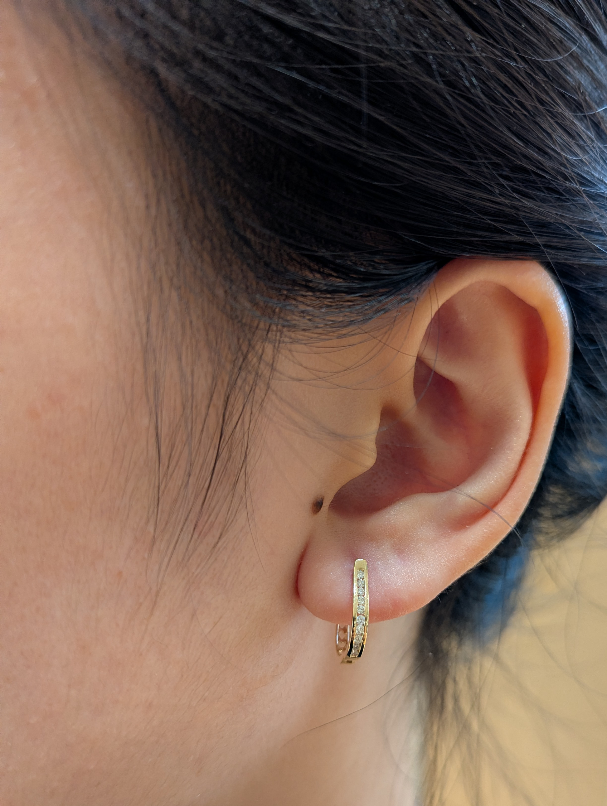 10K yellow gold 0.11 cttw Canadian diamond channel-set huggie hoop earring on ear model.