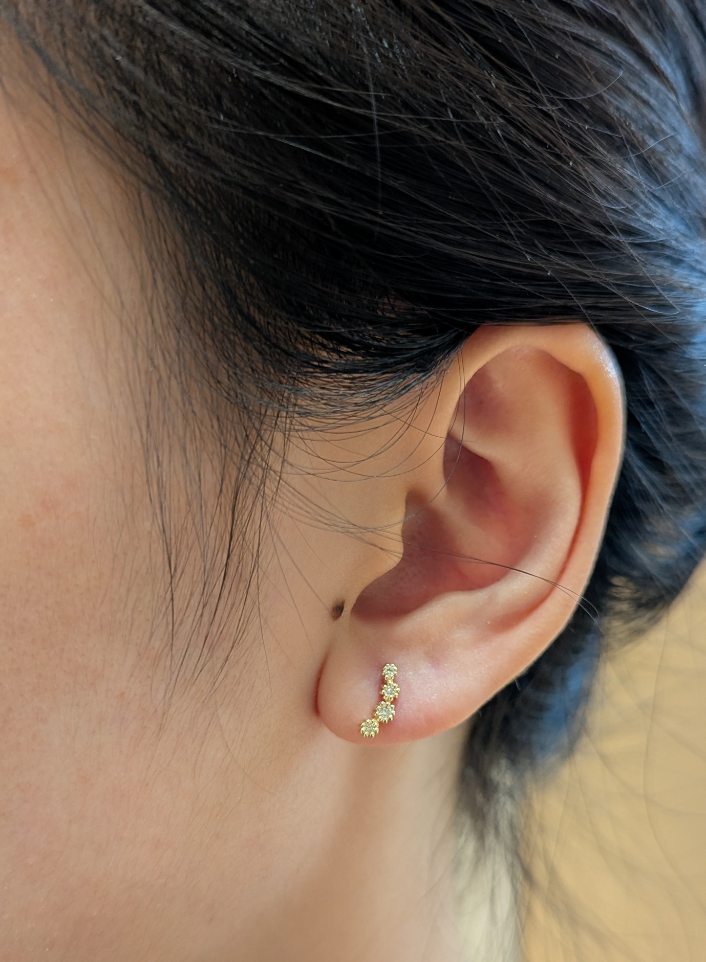 Model wearing a 10K yellow gold diamond ear climber earring with four graduated round brilliant cut Canadian diamonds along the earlobe.