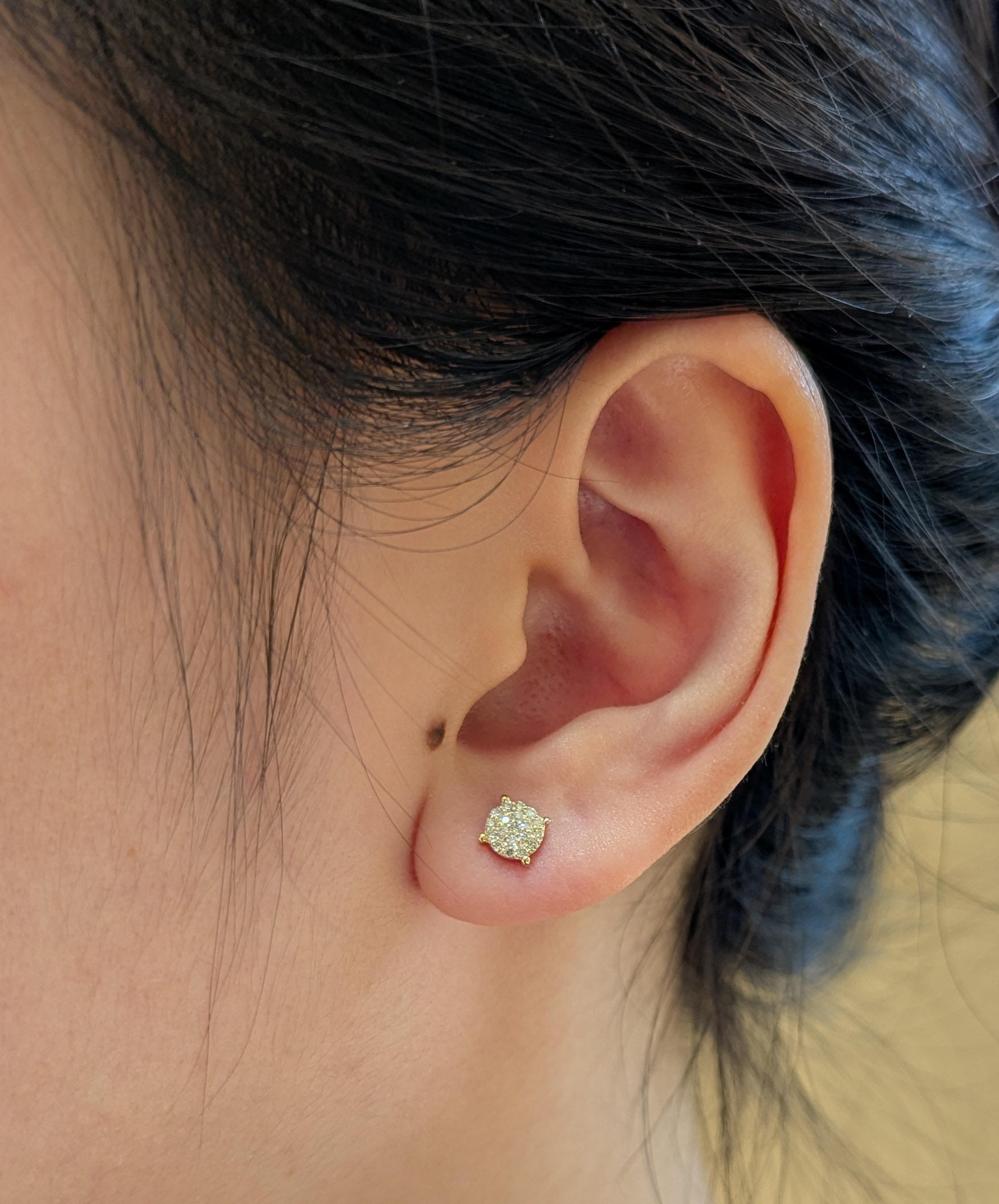 Close-up view of a 10K yellow gold round cluster stud earring featuring 0.10 cttw Canadian diamonds worn on a model's ear.