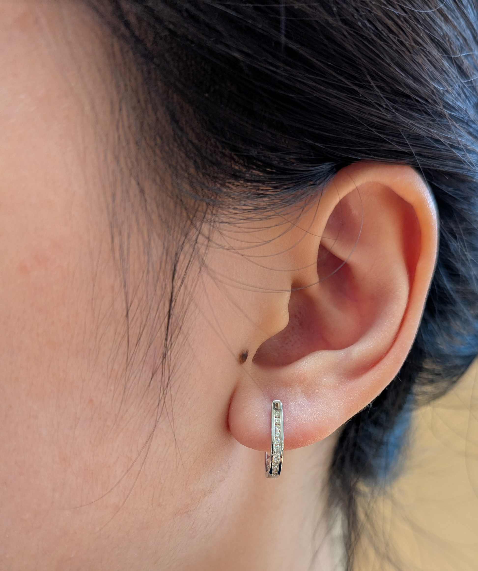 10K white gold 0.11 cttw Canadian diamond channel-set huggie hoop earring on ear model.