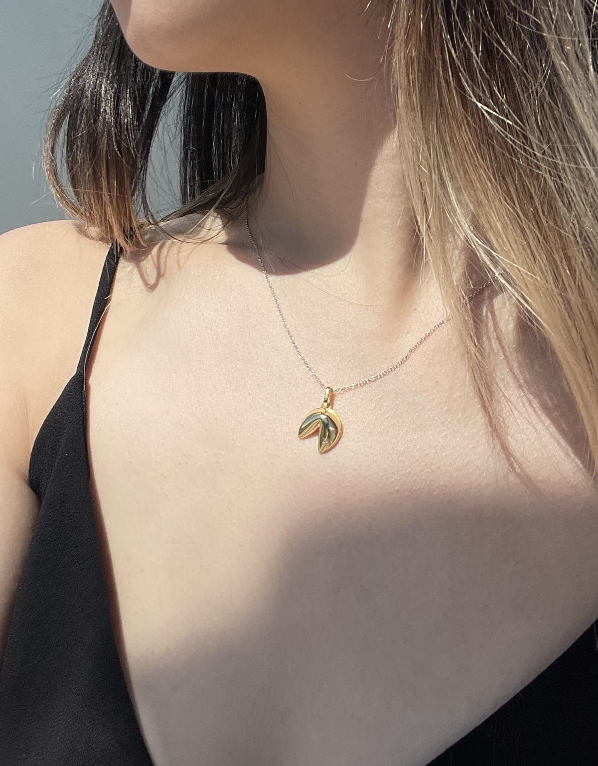 Close-up model photo showcasing a yellow gold plated 925 sterling silver fortune cookie pendant with silver rolo chain necklace on a neckline, highlighting the whimsical sculpted pendant accented with a 0.01 Ct natural Canadian diamond.