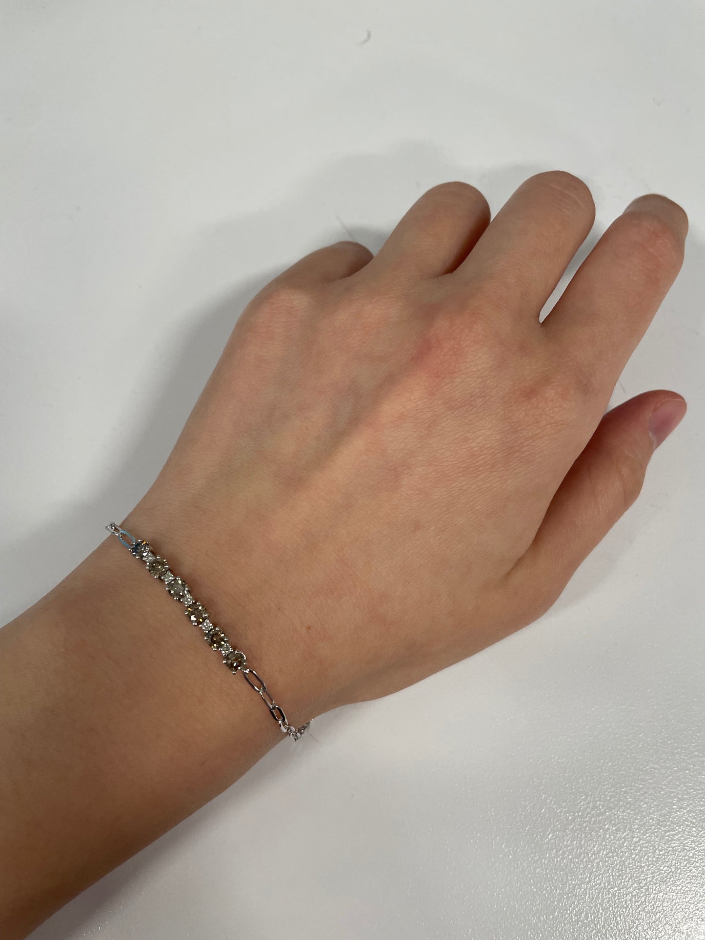 Close up of model wearing a 925 sterling silver paperclip bracelet featuring eleven Canadian diamonds on wrist. Five white diamonds and six warm coffee diamonds alternate along the center links, creating a patterned contrast.