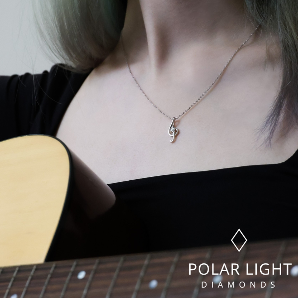 "Model wearing a silver treble clef pendant necklace with a central Canadian diamond, photographed with a guitar, featuring the Polar Light Diamonds brand logo