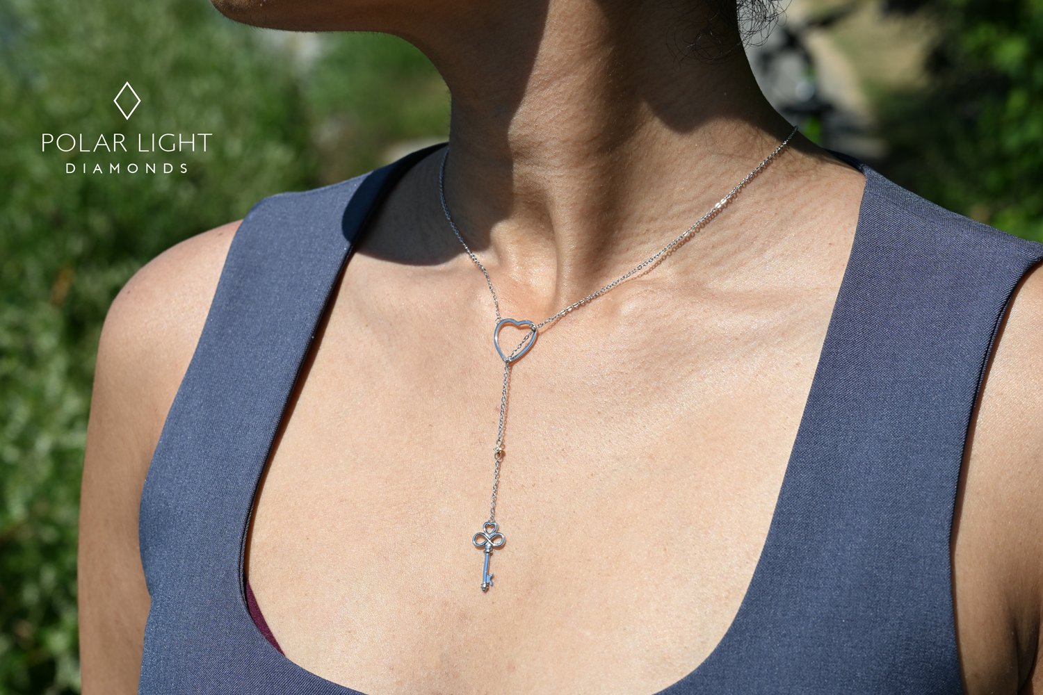 Person wearing a 925 sterling silver necklace with a heart and dangling 10k yellow gold diamond and key with heart and eternity detail design, outdoors.