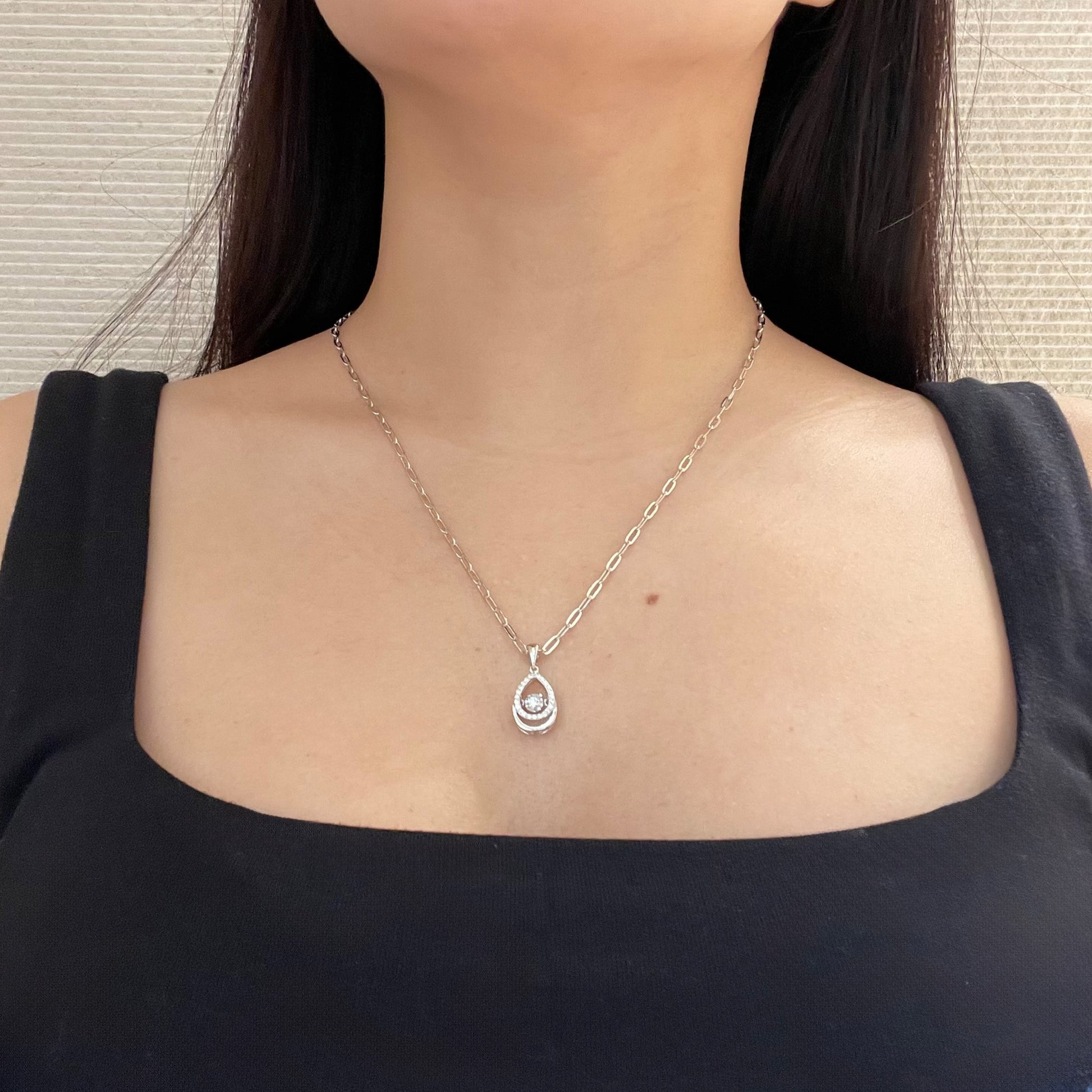 Model wearing a high-polish sterling silver paperclip necklace with a sophisticated teardrop pendant. The pendant features a 'dancing' miracle-set center Canadian diamond that moves with the wearer, surrounded by a halo of accent diamonds. This elegant lifestyle shot shows the necklace's length and modern, minimalist style.