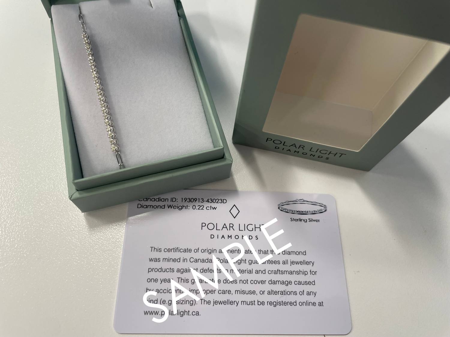 A luxury gift presentation of a 925 sterling silver paperclip link bracelet featuring a 0.22 cttw Canadian diamond half tennis station. The jewelry is displayed nestled inside an open, elegant green gift box, next to the box cover with the black Polar Light Diamonds brand logo, accompanied by an authentic Canadian diamond identification certificate sample.