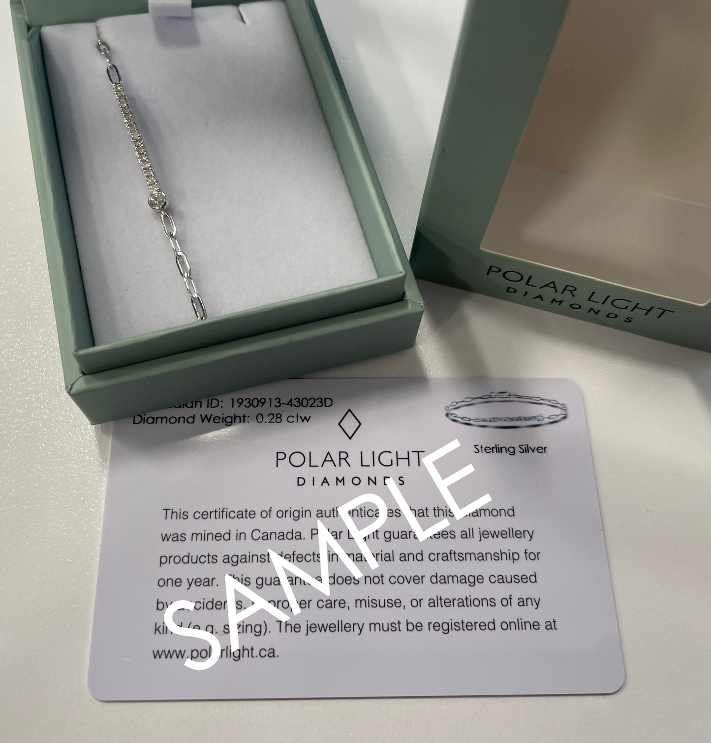 A product presentation and authenticity display for a Polar Light Diamonds bracelet. A sterling silver paperclip chain bracelet featuring a 0.28 cttw Canadian diamond half tennis station is nestled inside an open, sage green gift box. The signature outer box lid sits alongside it showing the brand logo, positioned above a white Polar Light Diamonds certificate of origin sample that details its ethical Canadian origin and product specifications.