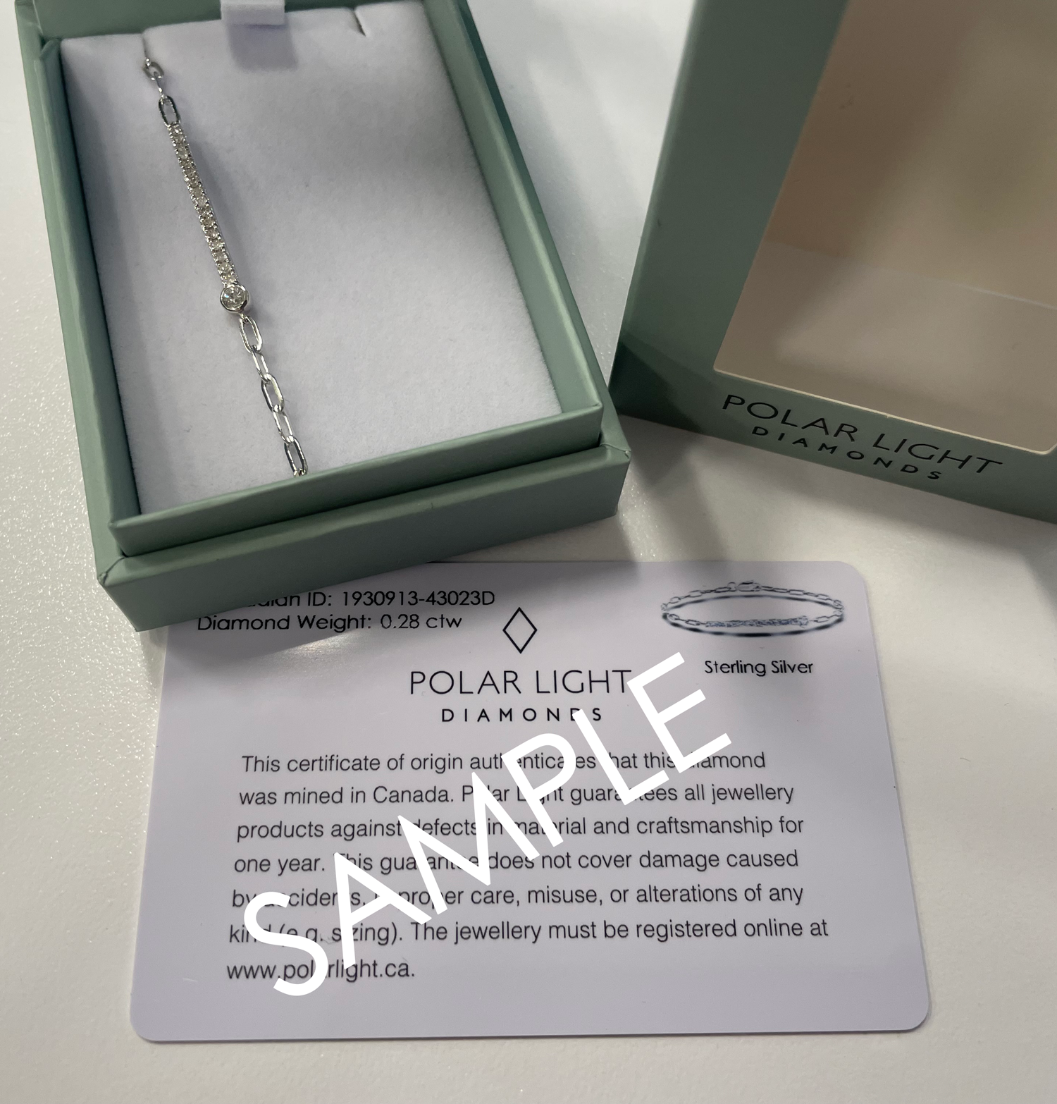 A product presentation and authenticity display for a Polar Light Diamonds bracelet. A sterling silver paperclip chain bracelet featuring a 0.28 cttw Canadian diamond half tennis station is nestled inside an open, sage green gift box. The signature outer box lid sits alongside it showing the brand logo, positioned above a white Polar Light Diamonds certificate of origin sample that details its ethical Canadian origin and product specifications.