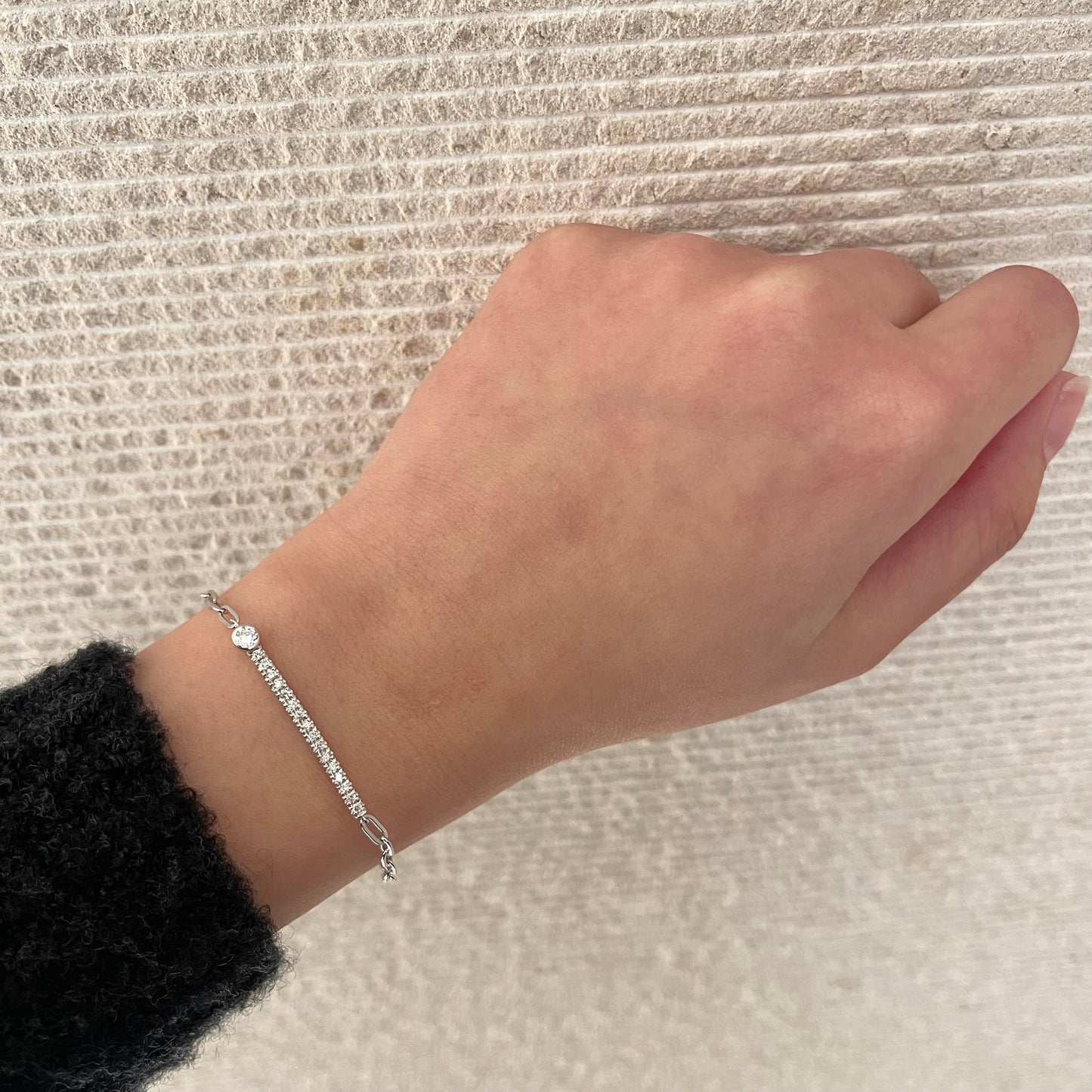 Close up of model wearing a high polish  paperclip 925 sterling silver line bracelet featuring  0.28 carat total weight natural Canadian diamonds on a textured beige background, showcasing a modern, minimalistic look.