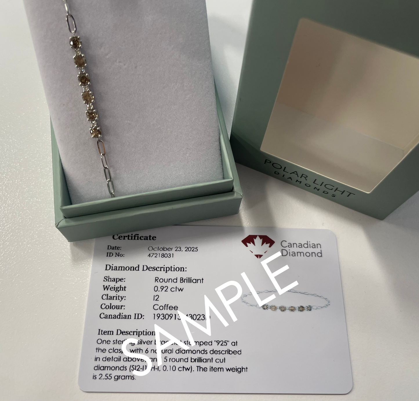 A product presentation and authenticity display for a coffee diamond Polar Light Diamonds bracelet. A 925 sterling silver paperclip chain bracelet featuring a striking row of six round brilliant-cut natural coffee-colored diamonds alternated with five small white diamond accents is beautifully displayed inside an open, sage green gift box. The branded outer gift box lid sits alongside it, positioned directly above a white Canadian Diamond certificate of origin sample.