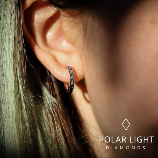 Close-up lifestyle view of a model wearing 10K white gold channel-set hoop earrings. The design features alternating natural blue sapphires and sparkling Canadian diamonds. The 'Polar Light Diamonds' logo is featured, emphasizing the premium craftsmanship and Canadian heritage of the brand.
