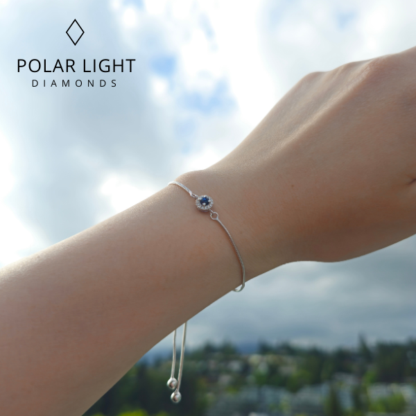 Bolo bracelet with a sapphire and halo Canadian diamond design on a wrist against a blurred outdoor background, featuring the brand 'Polar Light Diamonds'.