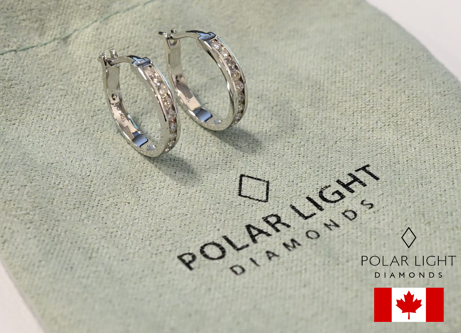 Close-up of 10K White Gold 1/5 Cttw Diamond 1.4cm petite channel-set hoop earrings with hinged latch backs, resting on a branded polar light fabric pouch.