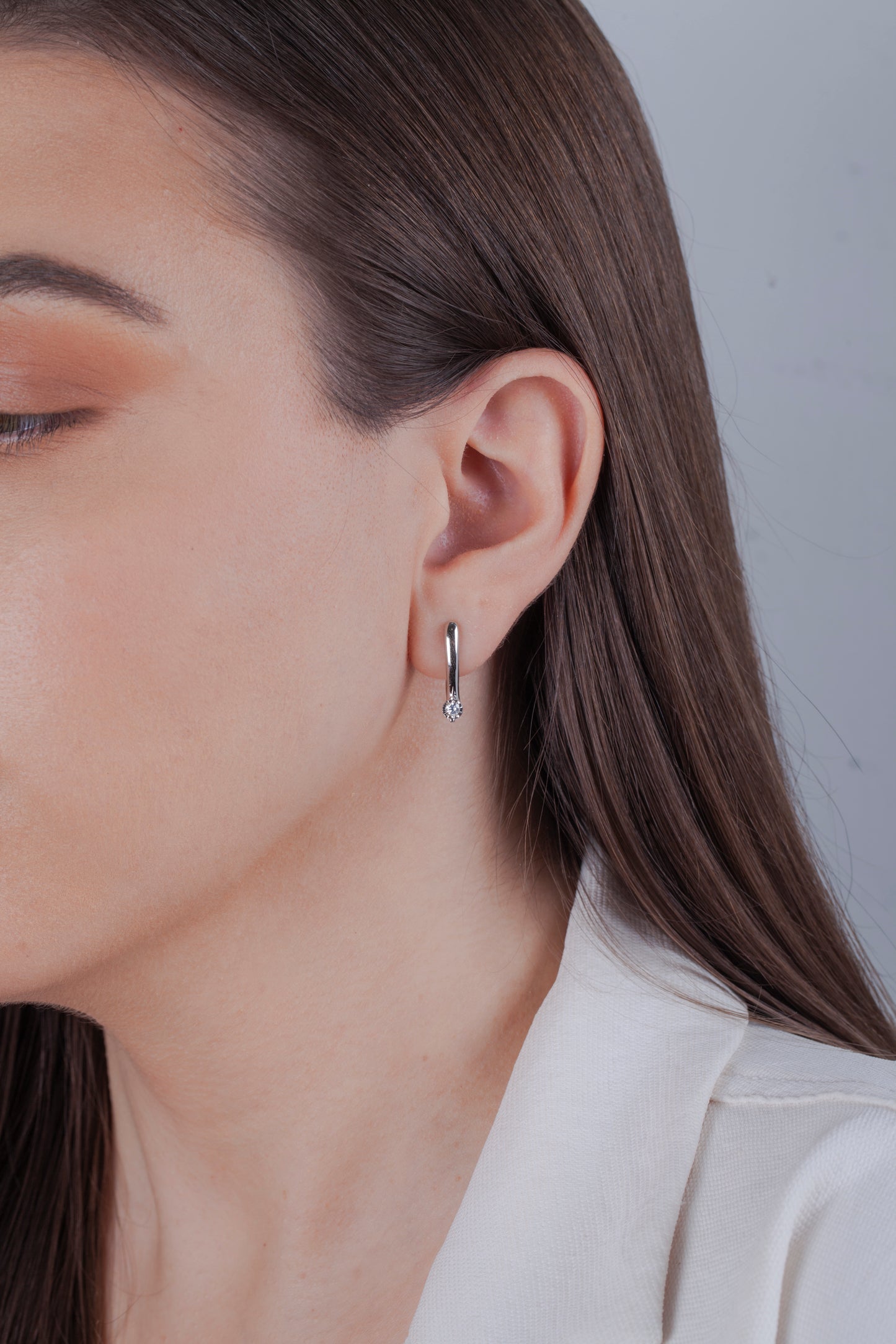 Close-up of a person wearing a silver hoop earring with a single natural diamond in a miracle setting at the bottom.