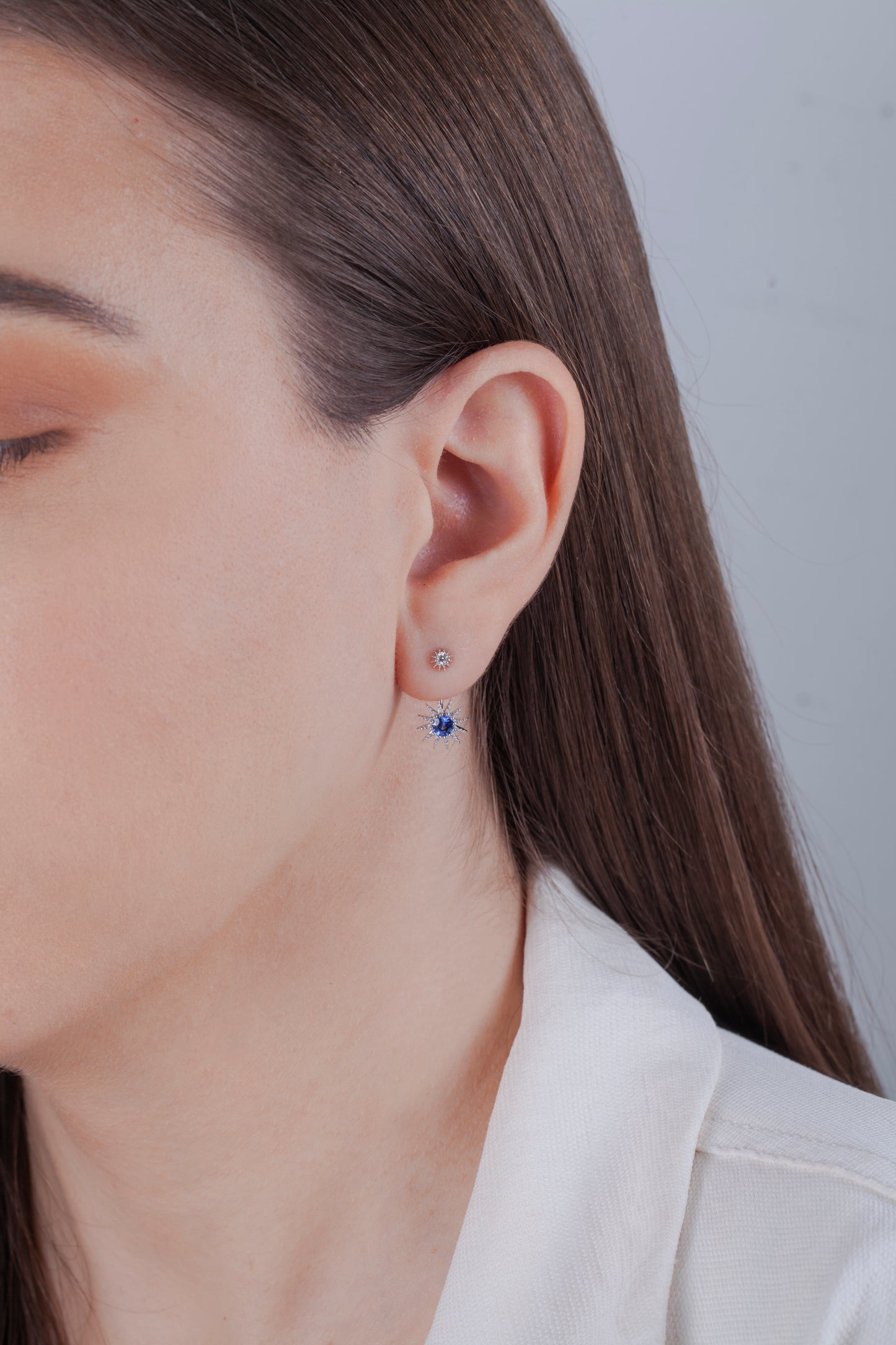 Close-up of a model wearing a starburst design dangle earring with diamond and sapphire on a plain background