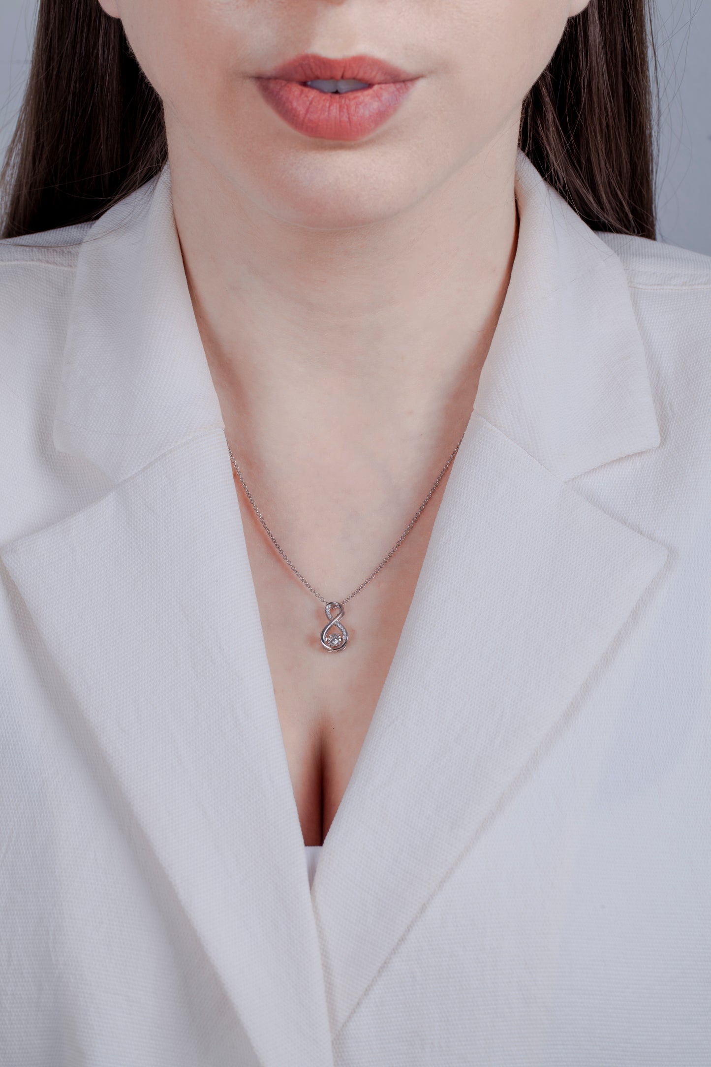 Person wearing a white blazer with a 925 sterling silver necklace featuring a infinity symbol shaped diamond charm.