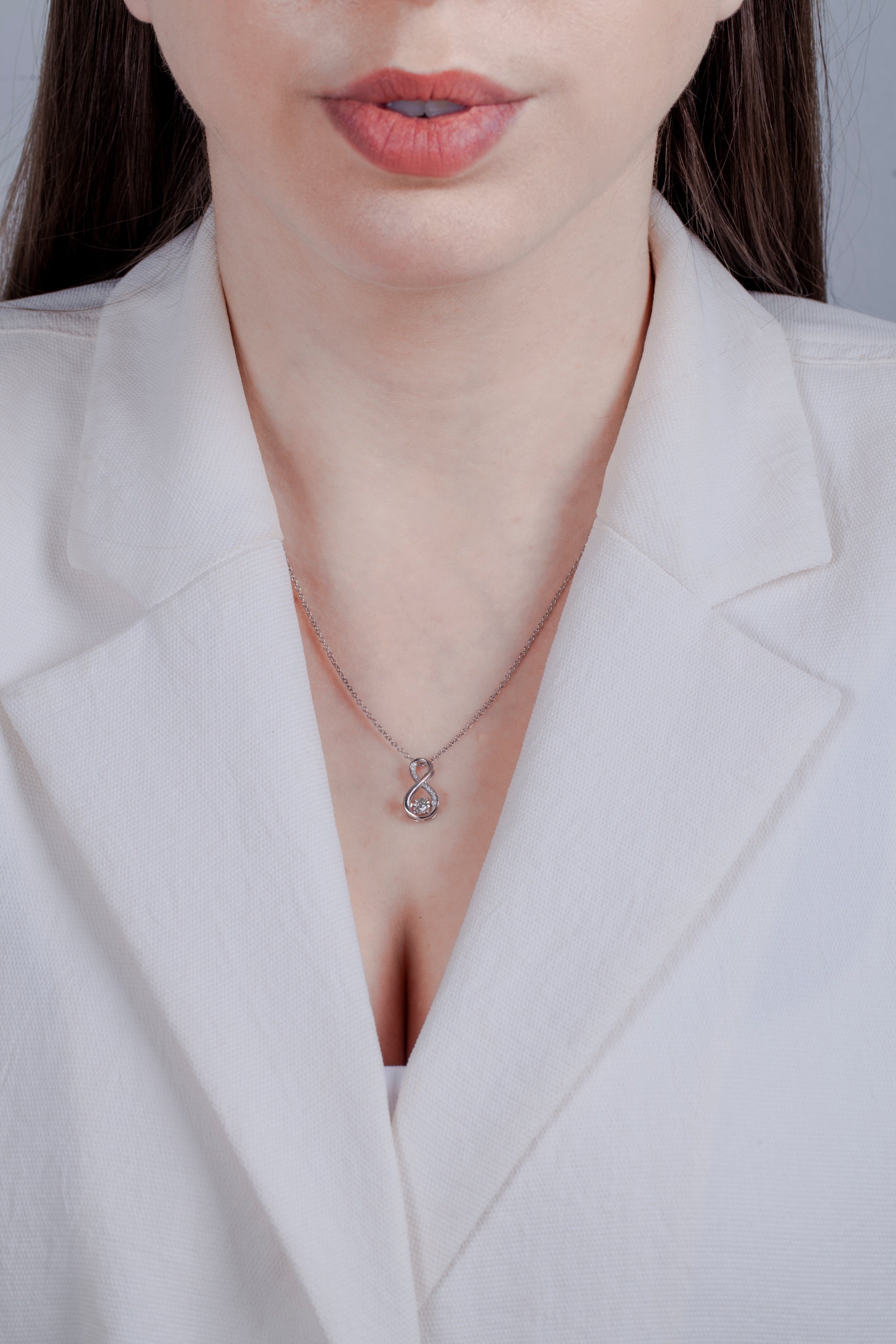 Person wearing a white blazer with a 925 sterling silver necklace featuring a infinity symbol shaped diamond charm.