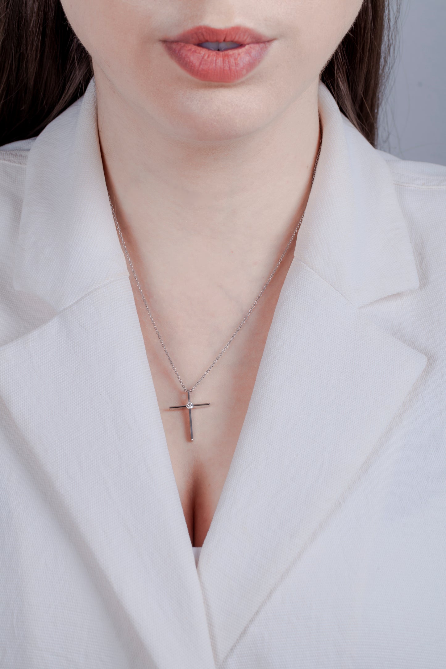 925 sterling silver Canadian diamond cross pendant on a model. Minimalist jewelry styling featuring a dainty silver cross and rolo chain with a professional white outfit.