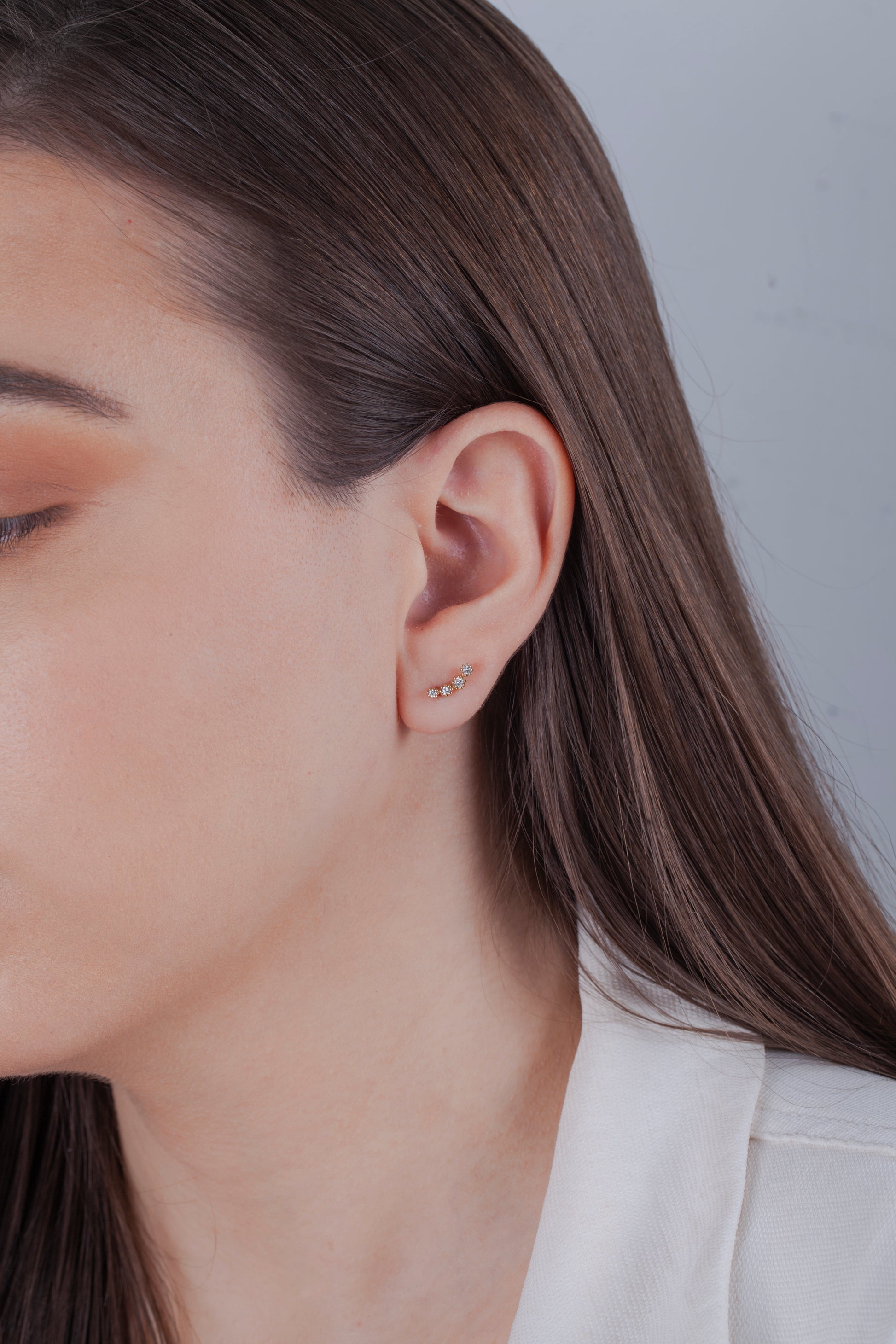 Close-up of a person wearing a gold diamond climber earring with a plain background