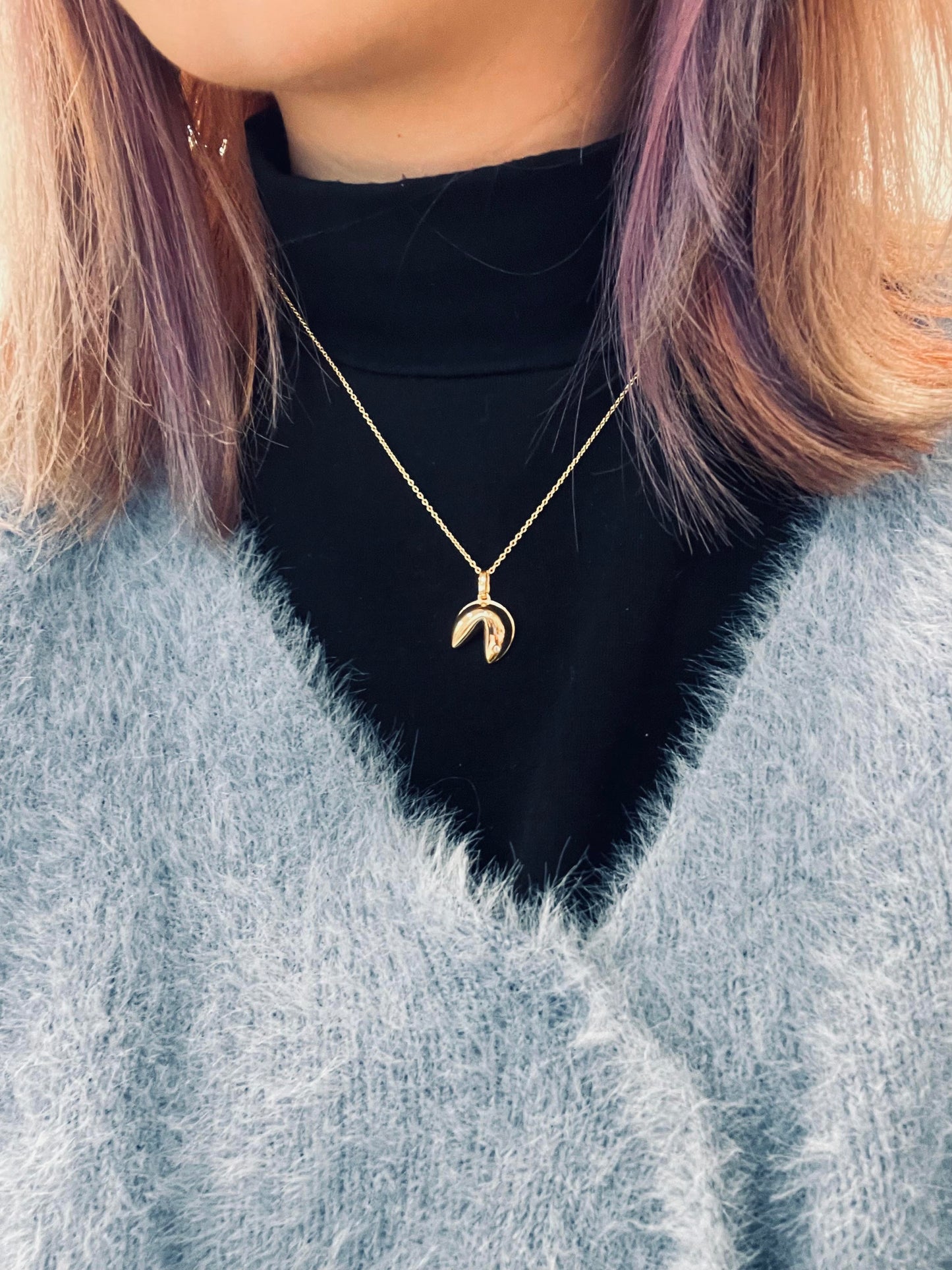 Model with dyed purple hair, black turtleneck and blue sweater wearing Canadian diamond fortune cookie charm on a rolo chain, showcasing a fun way of styling the pendant.