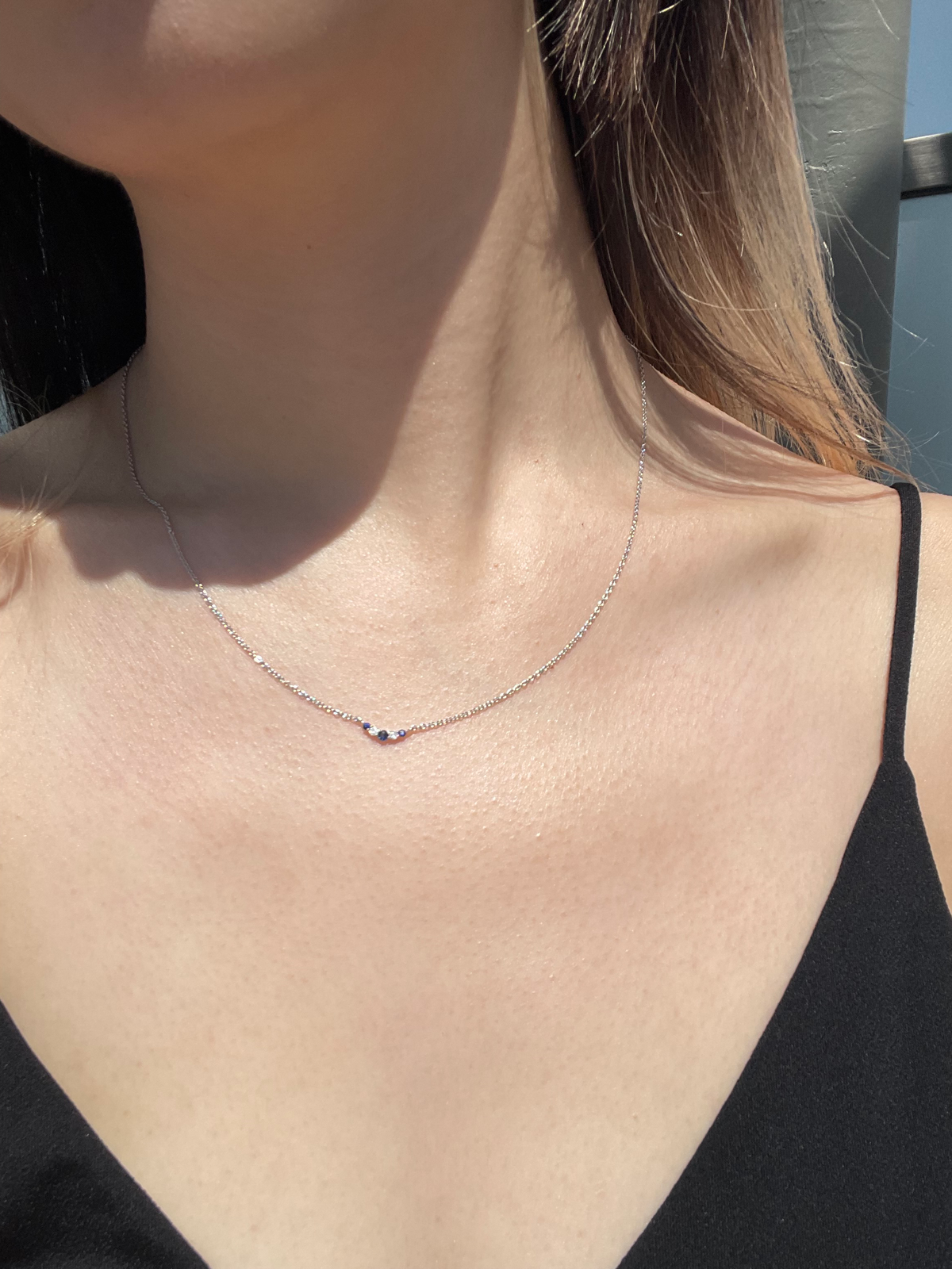 Close-up model photo showcasing a 925 sterling silver V-shaped curve necklace on a neckline, highlighting the 3mm delicate station design featuring alternating round blue sapphires and round brilliant cut Canadian diamonds.
