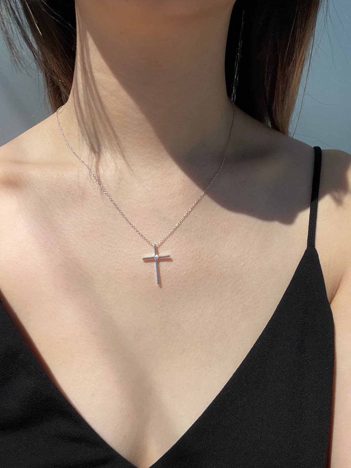 Close-up model photo showcasing a 925 sterling silver thin cross pendant necklace on a neckline, highlighting the minimalist frame draped on a delicate rolo chain with the 0.12 Ct natural Canadian diamond center stone catching the light.