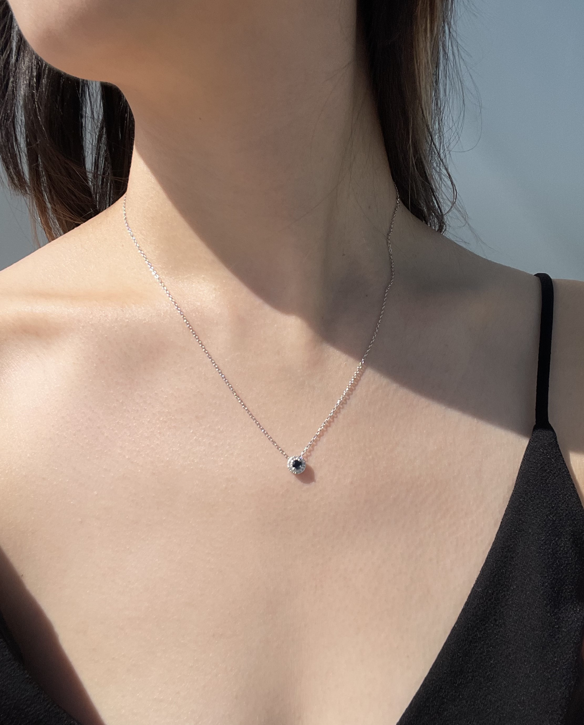 Close-up model photo showcasing a 925 sterling silver halo pendant necklace, featuring a 0.18 Carat round blue sapphire center stone surrounded by a brilliant 0.10 Cttw Canadian diamond halo on a delicate chain.