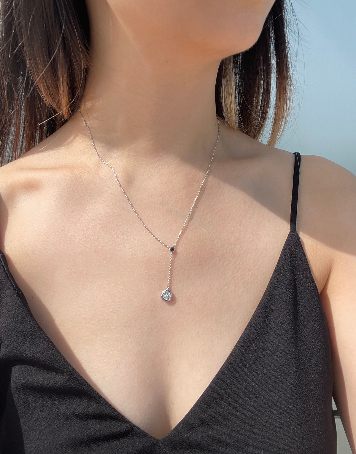 Close-up model photo showcasing a sterling silver Y-style necklace, featuring a small round blue sapphire accent at the junction and a dangling pear-shaped pendant with a miracle-set white diamond.