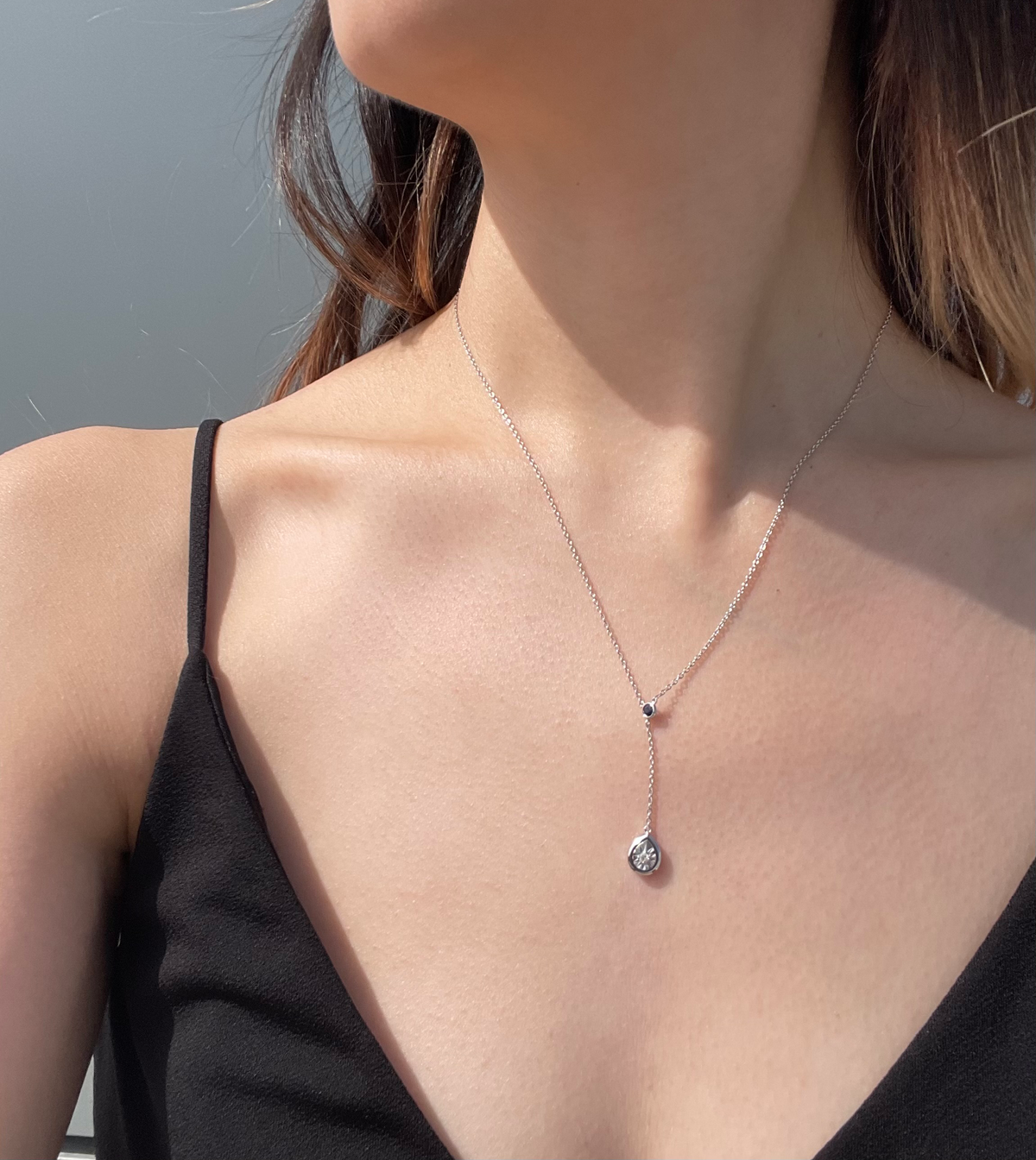 Close-up model photo showcasing a sterling silver Y-style necklace, featuring a small round blue sapphire accent at the junction and a dangling pear-shaped pendant with a miracle-set white diamond.