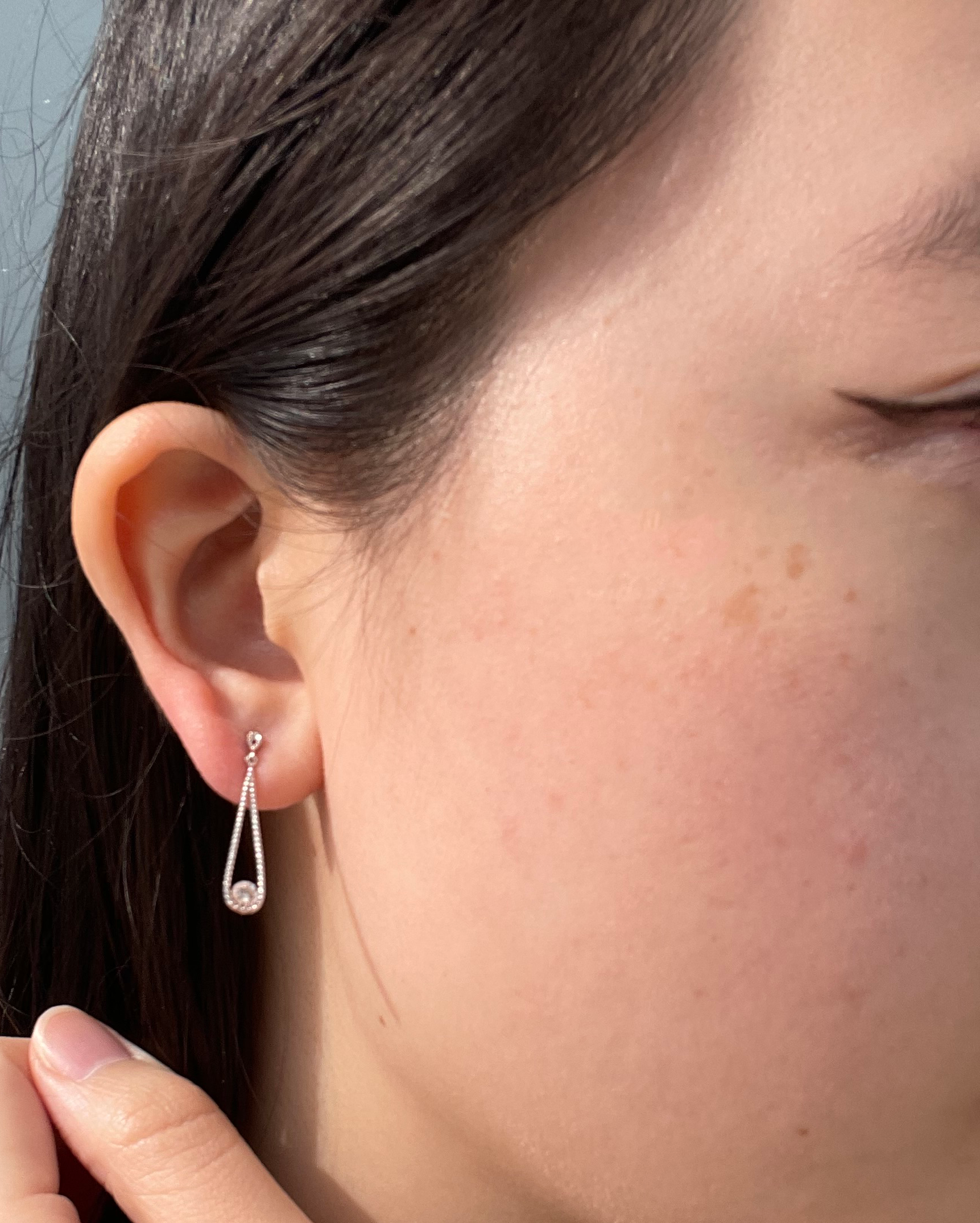 Close-up model photo showcasing a 925 sterling silver droplet dangle earring, featuring an open teardrop design lined with a milgrain border and a 0.06 Cttw Canadian diamond in a miracle setting.