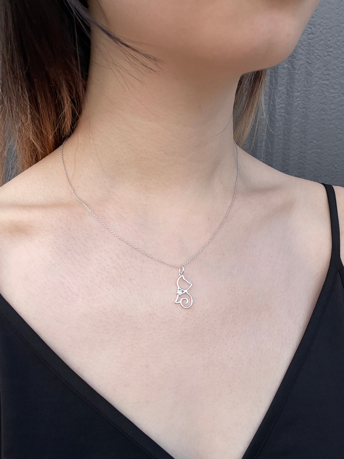Detailed view of a sterling silver cat-shaped silhouette pendant, featuring a subtle Canadian diamond accent and suspended from a fine, reflective rolo chain against a black top.