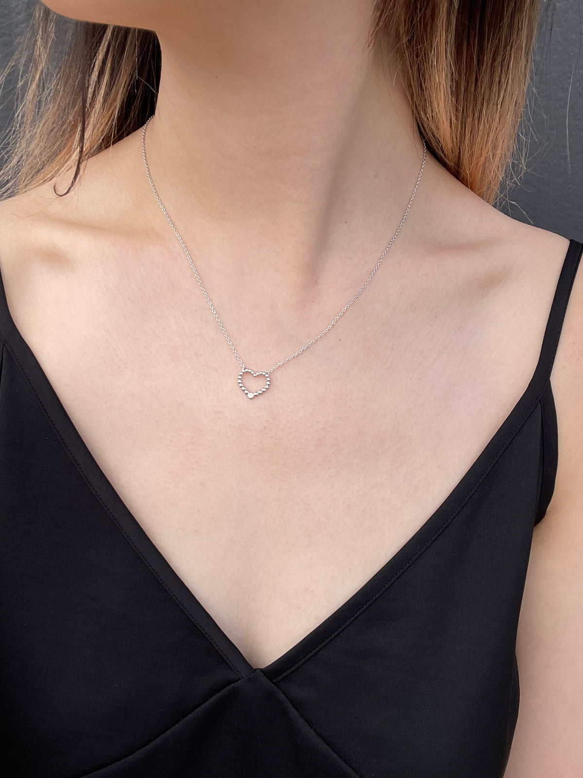 Close-up shot of a model wearing a high-polish sterling silver bubble heart pendant, featuring a subtle, shimmering Canadian diamond, suspended from a delicate, light-reflecting rolo chain, set against a simple black slip dress.