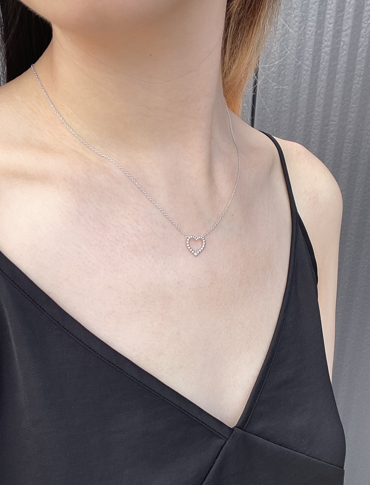 Close-up shot of a model wearing a high-polish sterling silver bubble heart pendant, featuring a subtle, shimmering Canadian diamond, suspended from a delicate, light-reflecting rolo chain, set against a simple black slip dress.