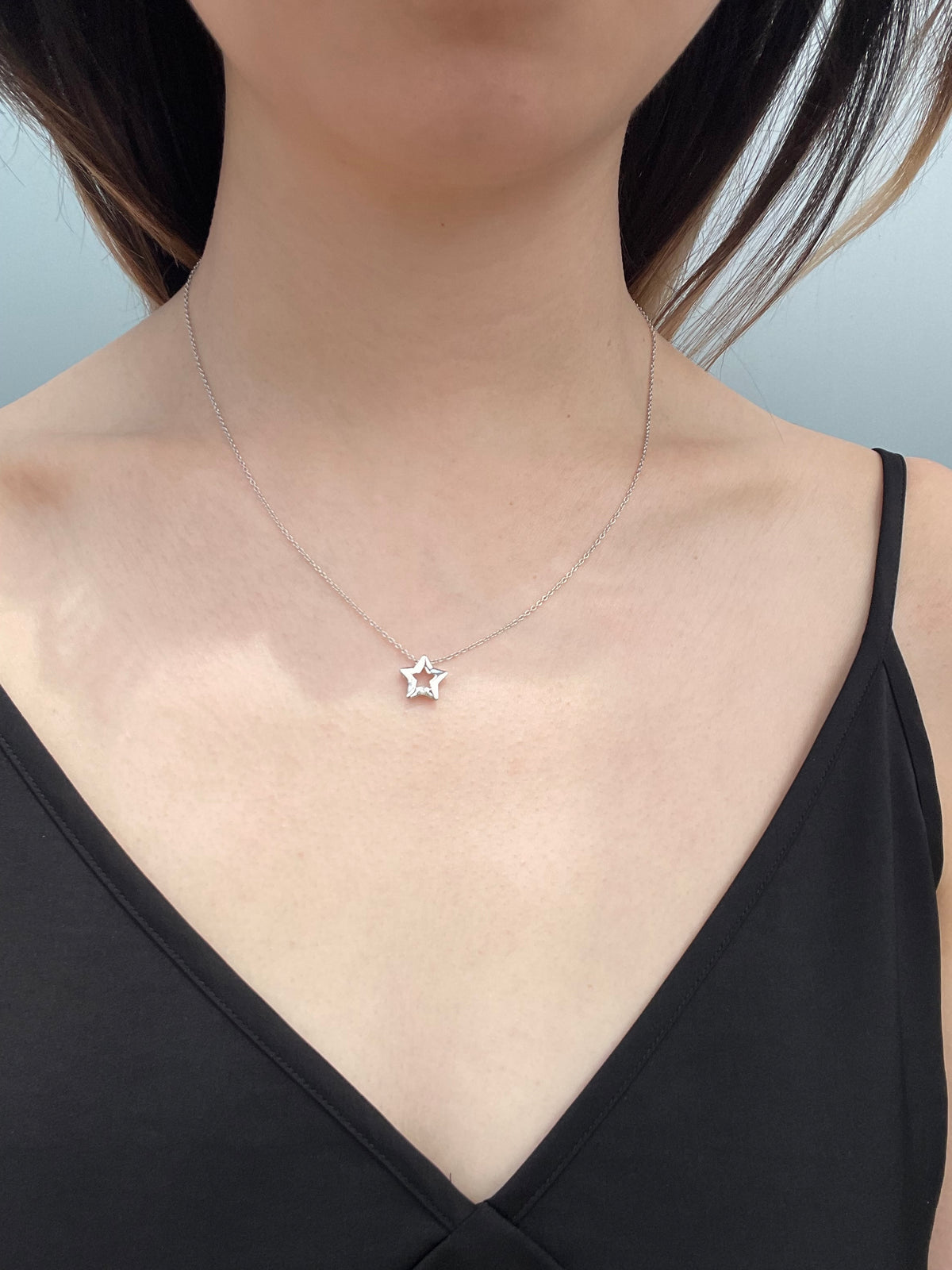 Close-up shot of a model wearing a high-polish sterling silver star-shaped pendant, featuring a subtle, shimmering Canadian diamond accent, suspended from a delicate, light-reflecting rolo chain, set against a simple black camisole.