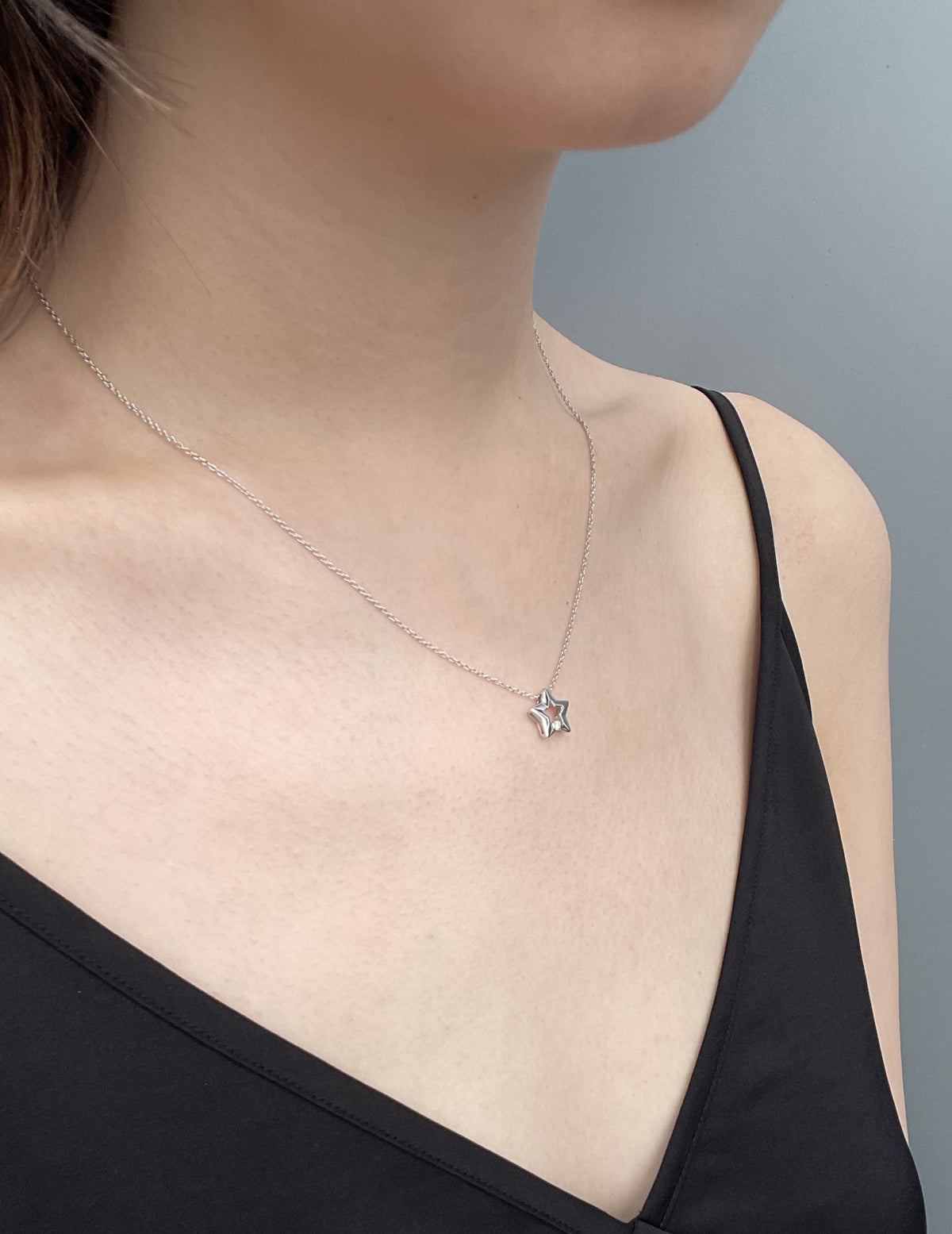 Close-up shot of a model wearing a high-polish sterling silver star-shaped pendant, featuring a subtle, shimmering Canadian diamond accent, suspended from a delicate, light-reflecting rolo chain, set against a simple black camisole.