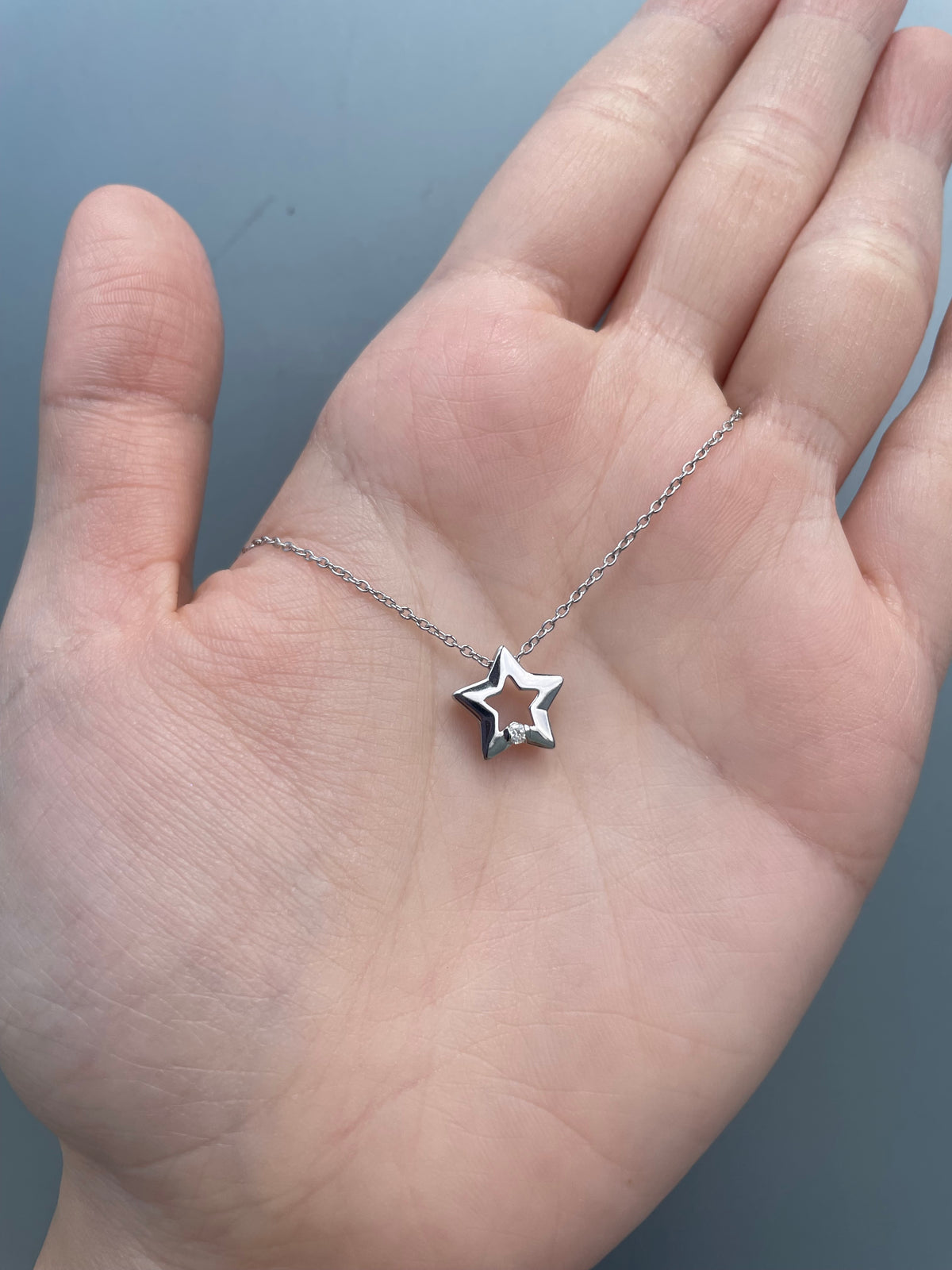 A crisp, hand-held view highlighting the high-polish finish of a sterling silver open-star pendant, focusing on the refined craftsmanship of the shimmering Canadian diamond and the delicate, light-reflecting links of the accompanying rolo chain.