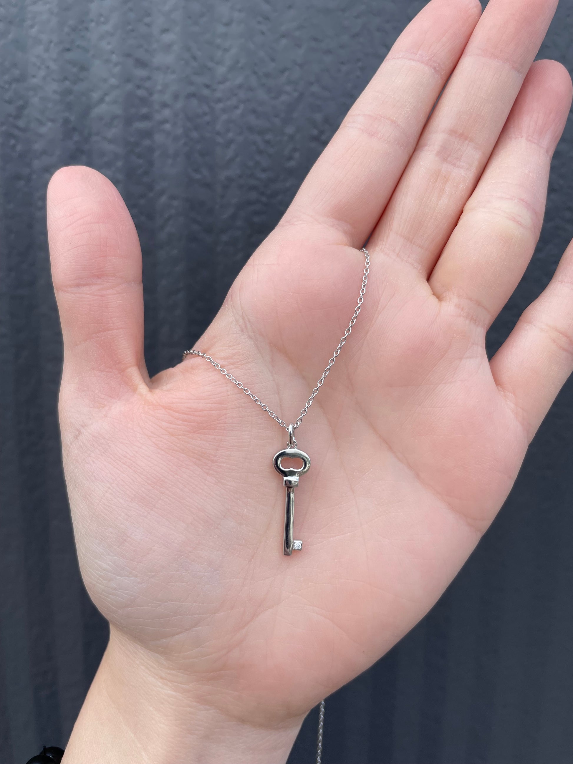 Hand held view of a sterling silver key-shaped pendant, featuring a genuine Canadian diamond accent and a delicate cable chain.