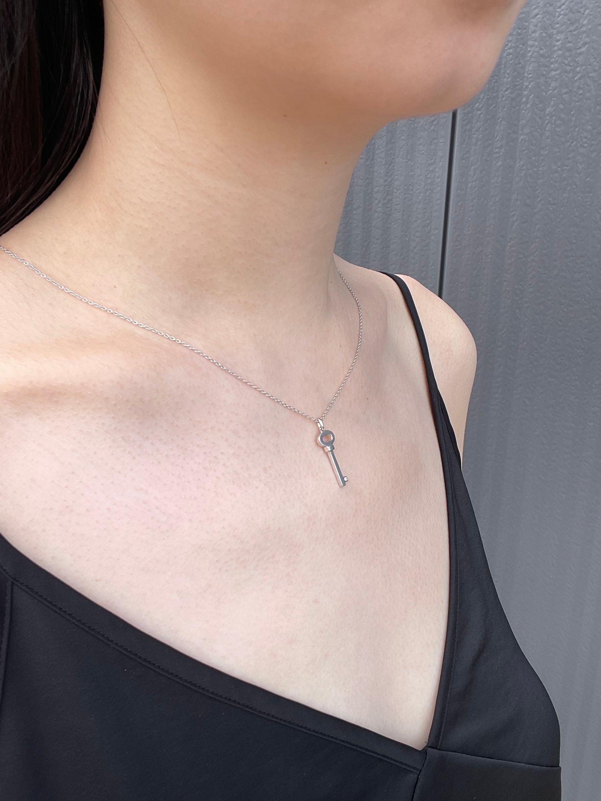 Model wearing a sterling silver key-shaped pendant necklace, featuring a subtle Canadian diamond accent and a delicate cable chain against a black top.