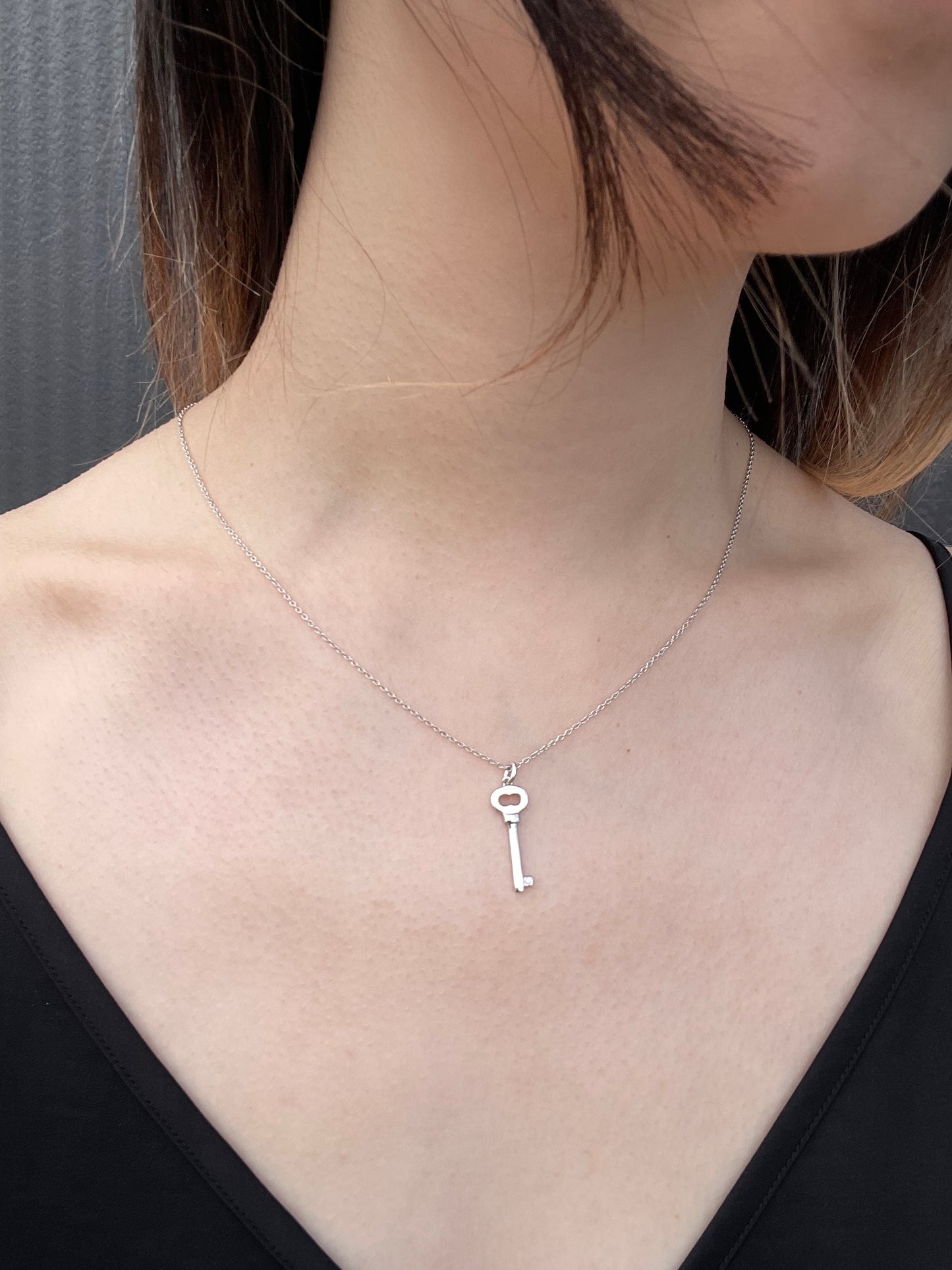 Model wearing a sterling silver key-shaped pendant necklace, featuring a subtle Canadian diamond accent and a delicate cable chain against a black top.