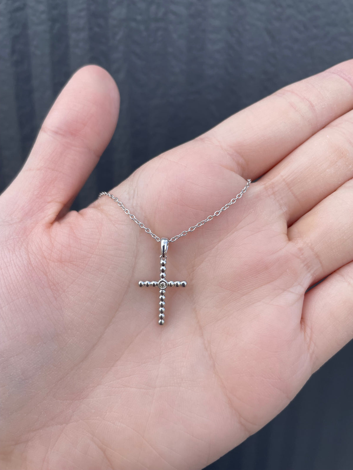Hand held view of a sterling silver beaded cross pendant, featuring a central Canadian diamond accent and a delicate rolo chain.