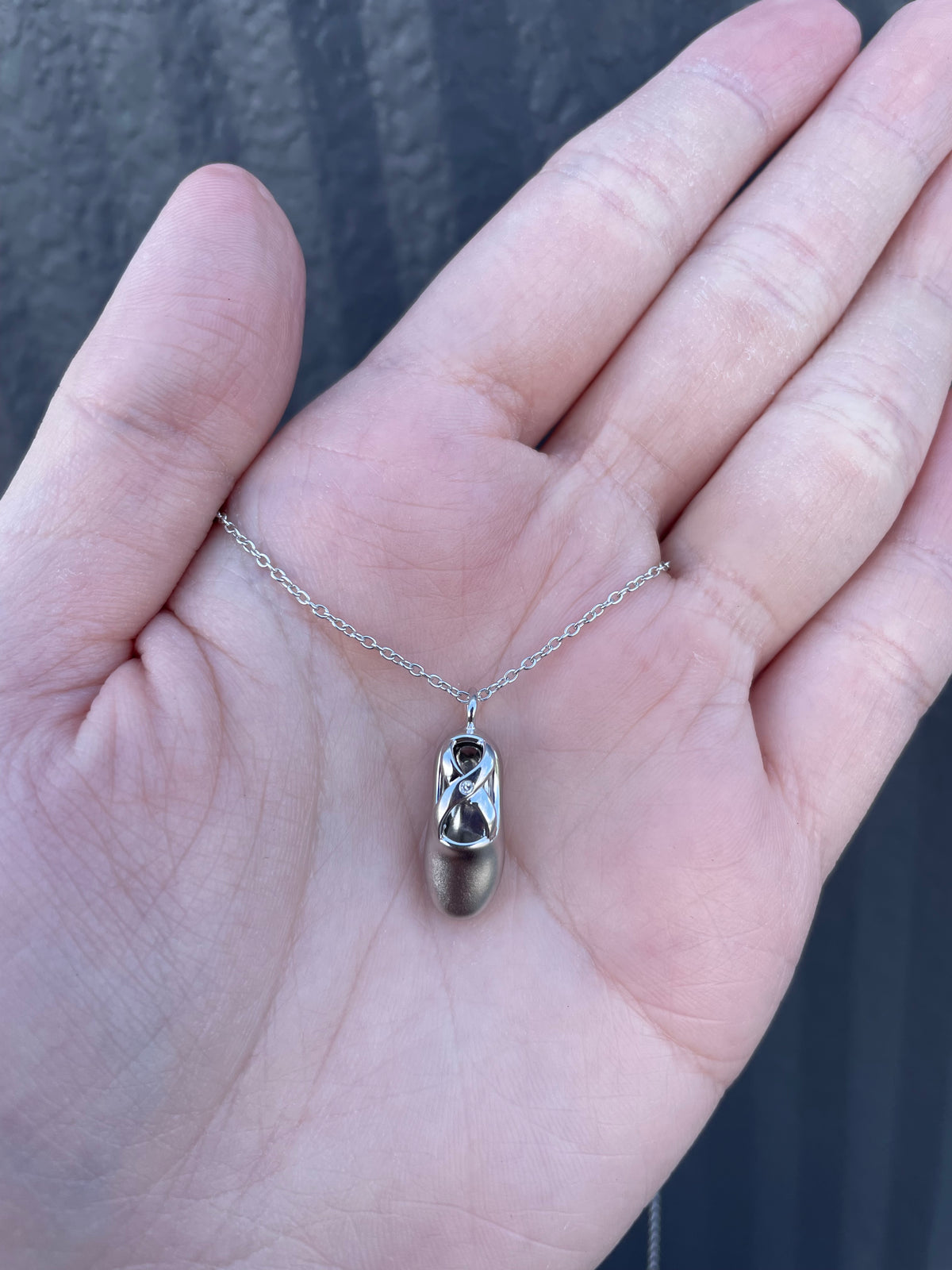 Close-up of a sterling silver ballet slipper charm, showcasing its intricate cut-out craftsmanship and elegant high-polish finish on a fine rolo chain.