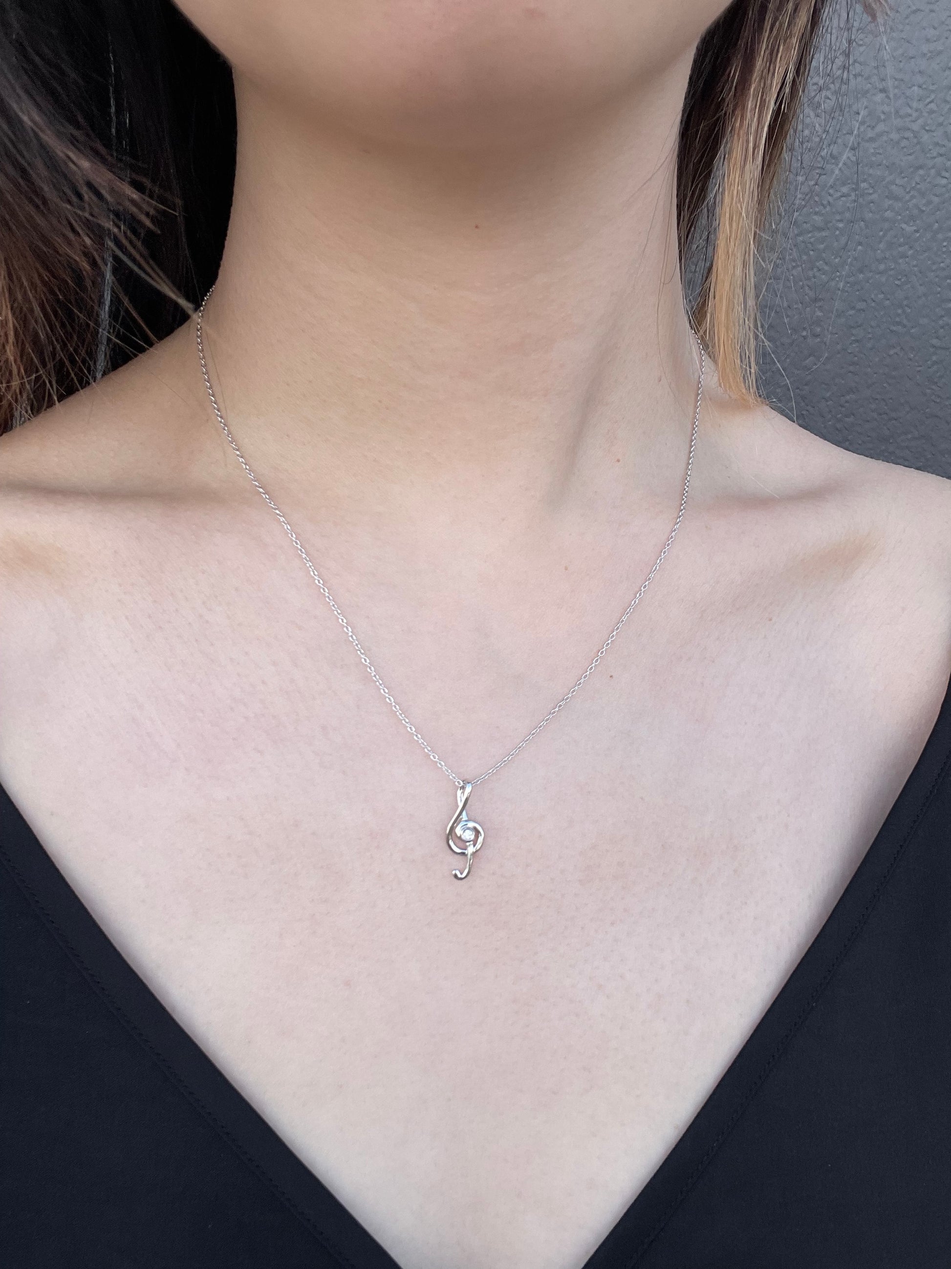 Model wearing a silver treble clef pendant necklace with a central Canadian diamond against a black top.