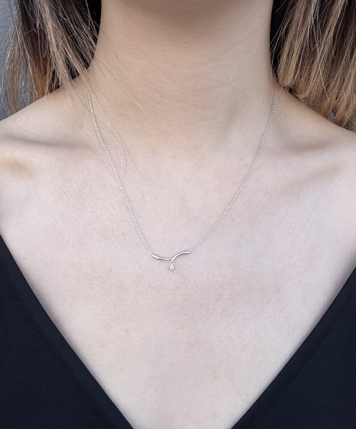 Model wearing a sterling silver wave necklace with a single Canadian diamond accent against a black top.