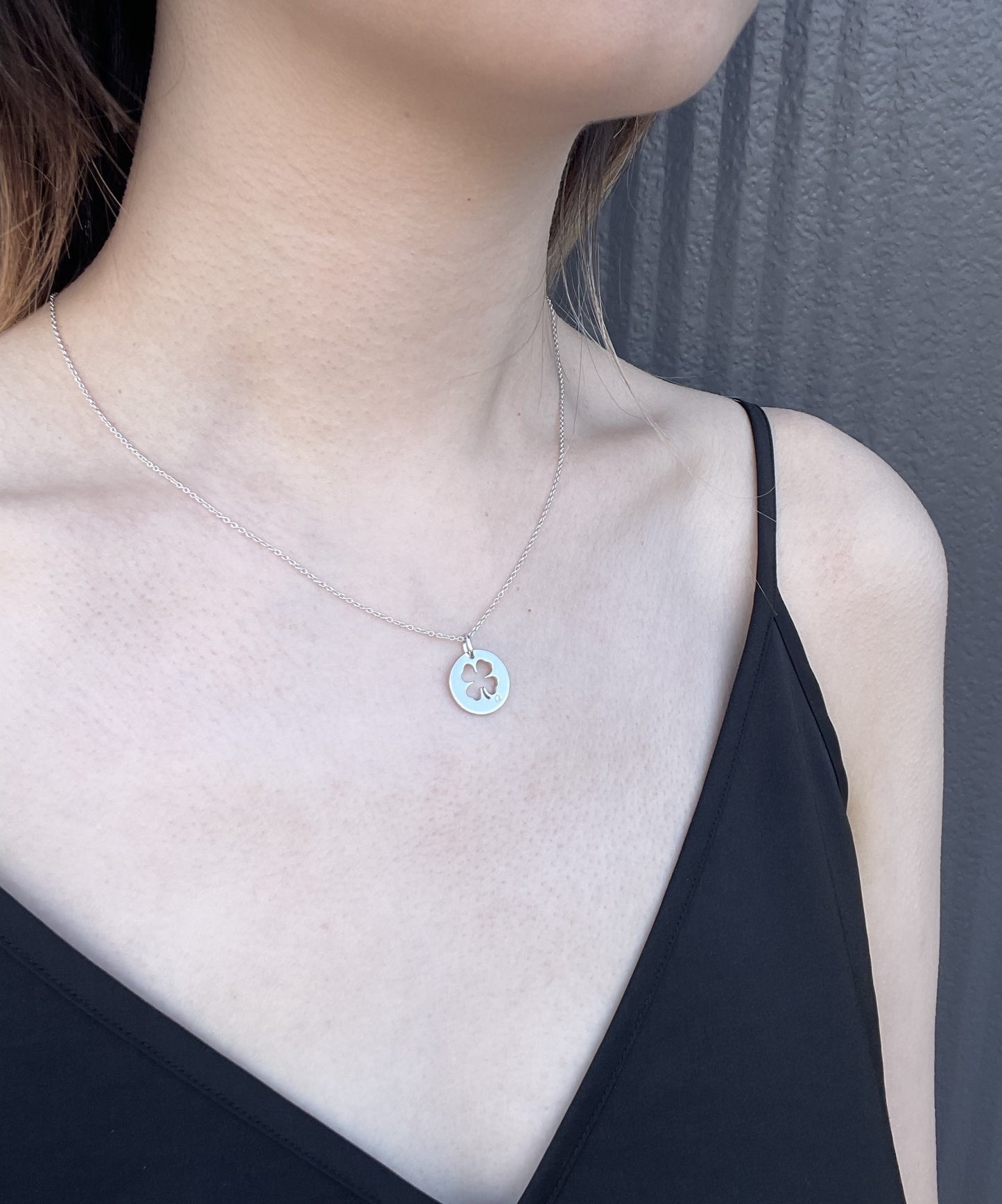 Close-up of a model wearing a high-polish sterling silver four-leaf clover pendant, featuring a cut-out design and a delicate, shimmering rolo chain, accented by a single round brilliant-cut Canadian diamond.