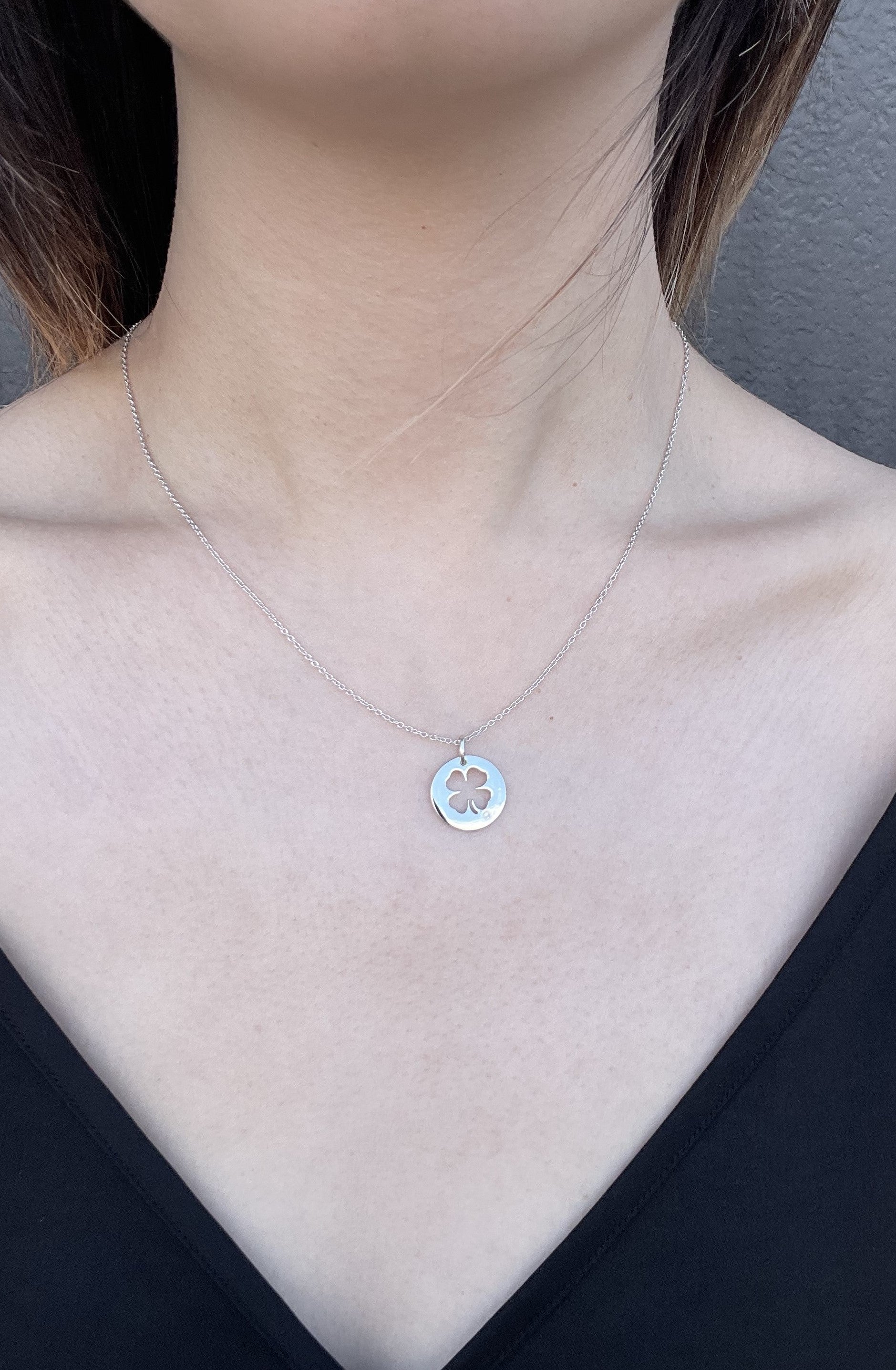 Close-up of a model wearing a high-polish sterling silver four-leaf clover pendant, featuring a cut-out design and a delicate, shimmering rolo chain, accented by a single round brilliant-cut Canadian diamond.